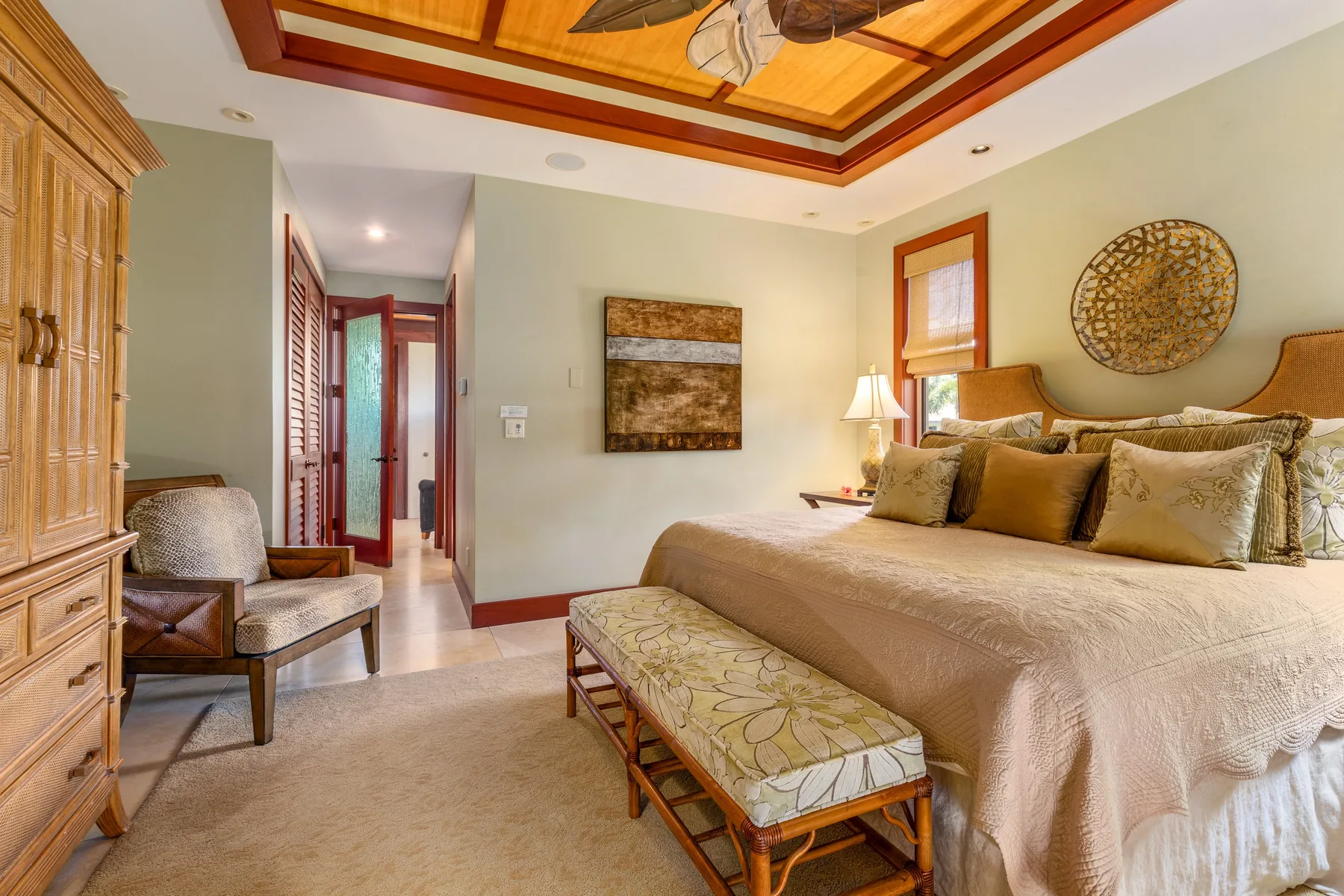 A bedroom with a large bed, upholstered bench, and wooden ceiling beams.