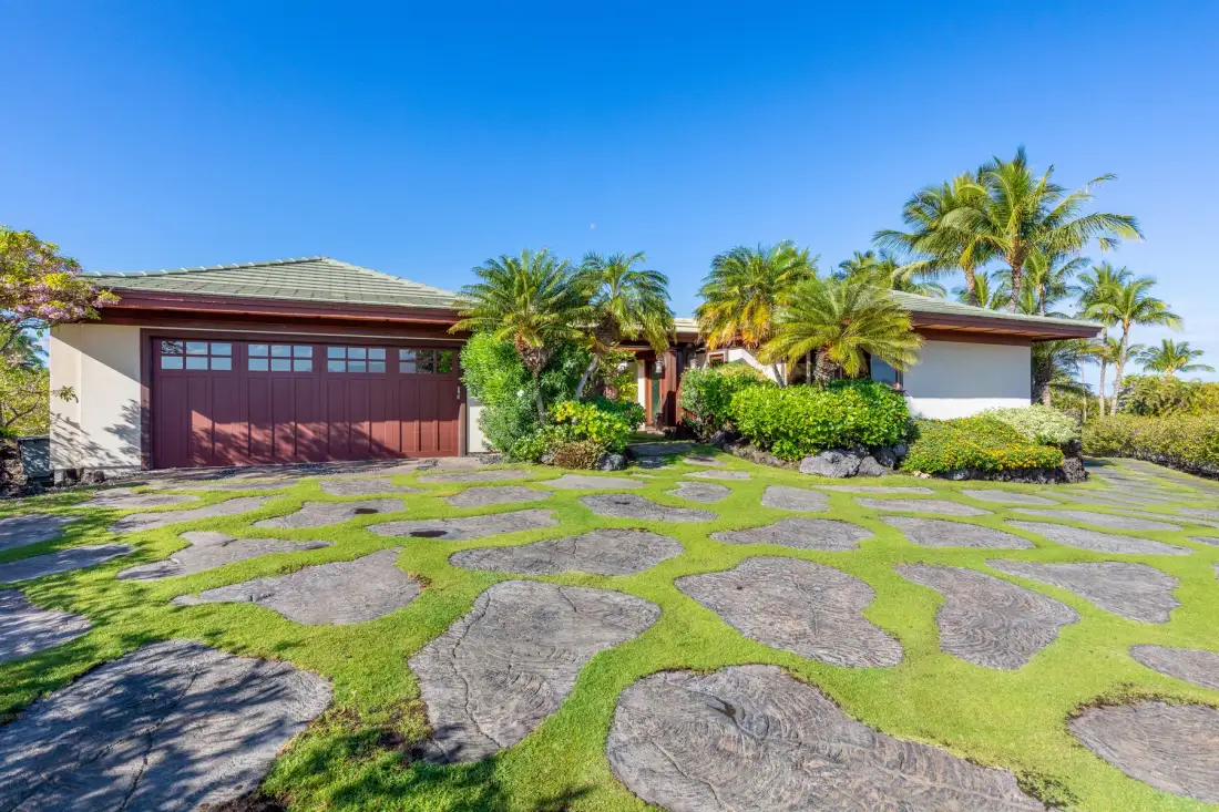 A single-story house with a broad driveway set among tropical palms.