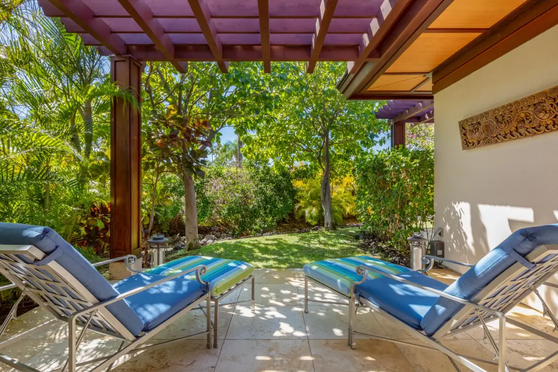 A garden patio with blue cushioned loungers beneath a wooden pergola.