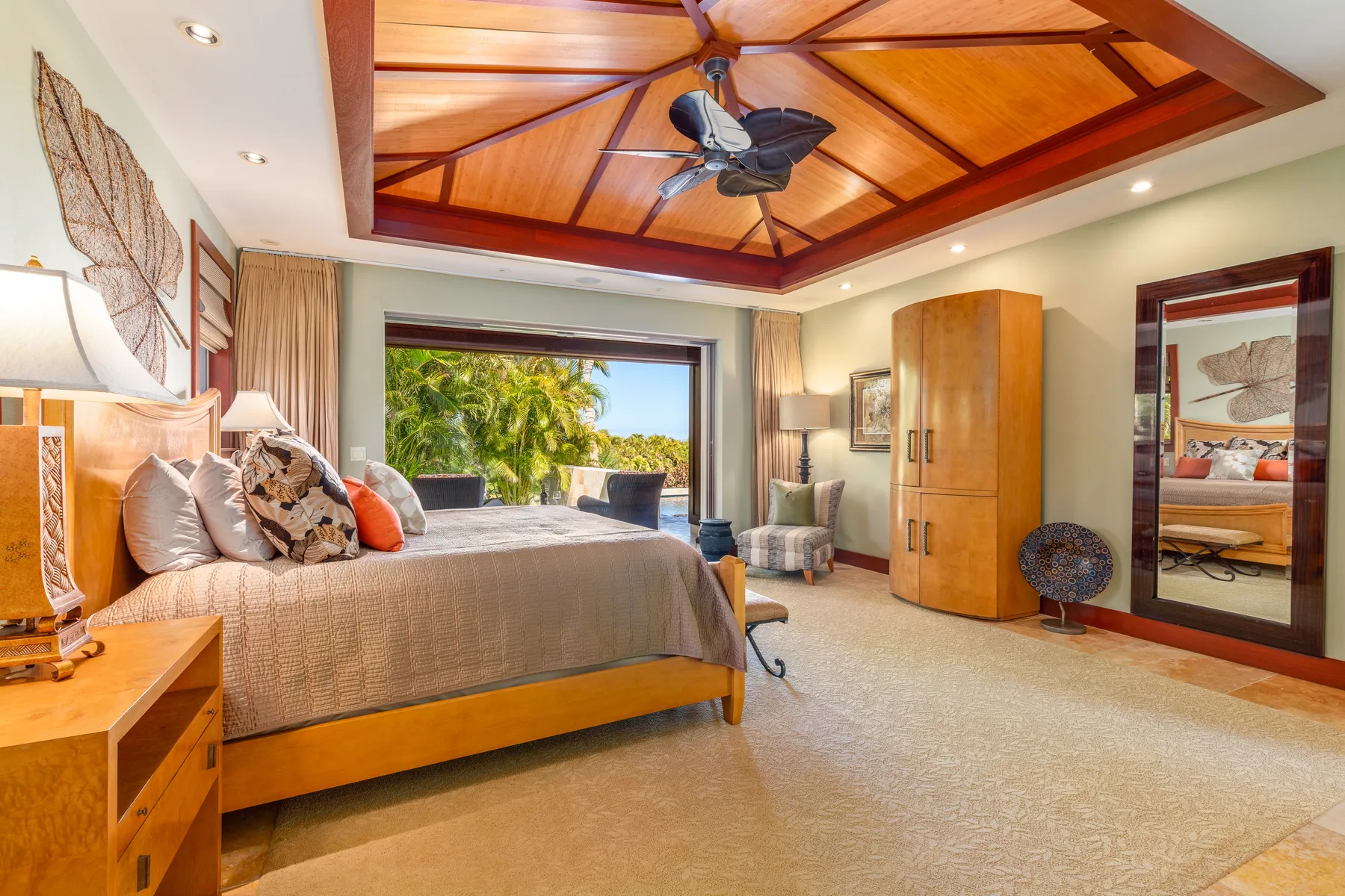 A bedroom with a large bed, wooden ceiling, and tropical greenery visible through the window.