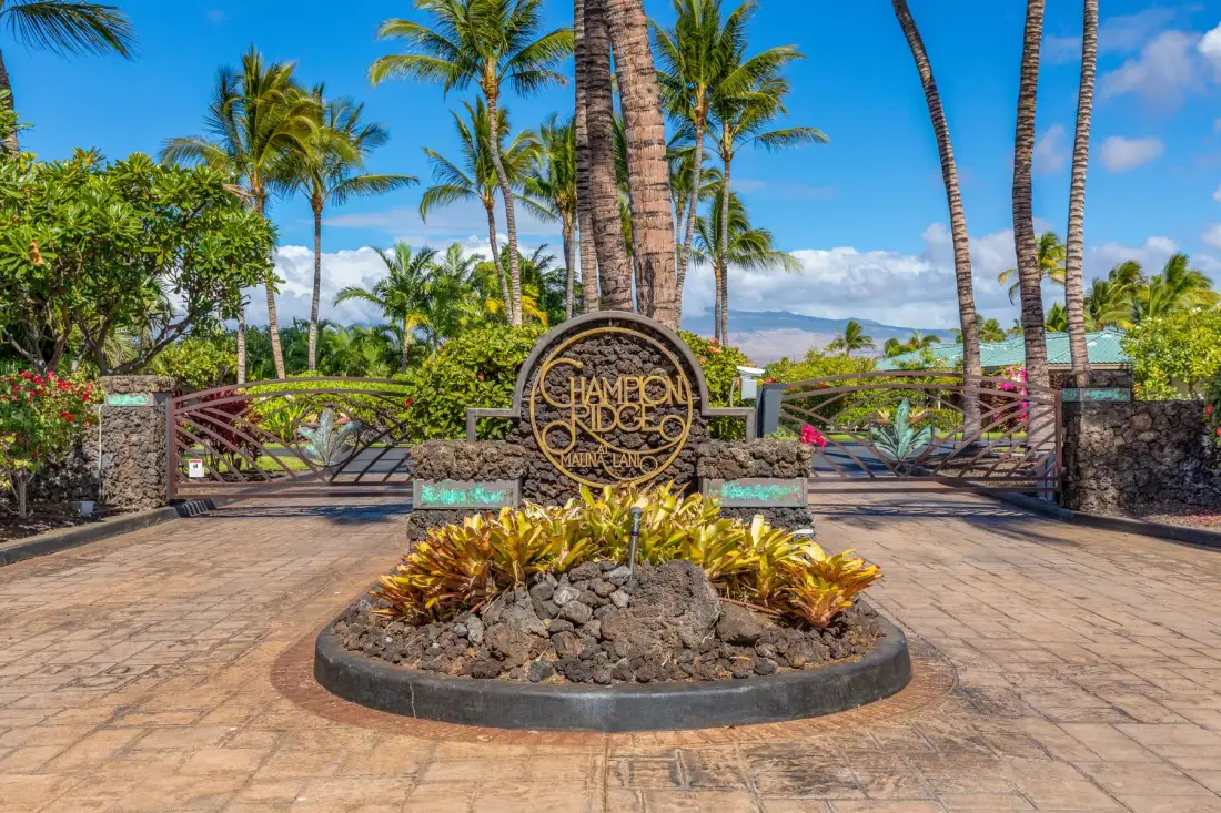 A landscaped entrance features a circular resort sign, palm trees, and a paved path.