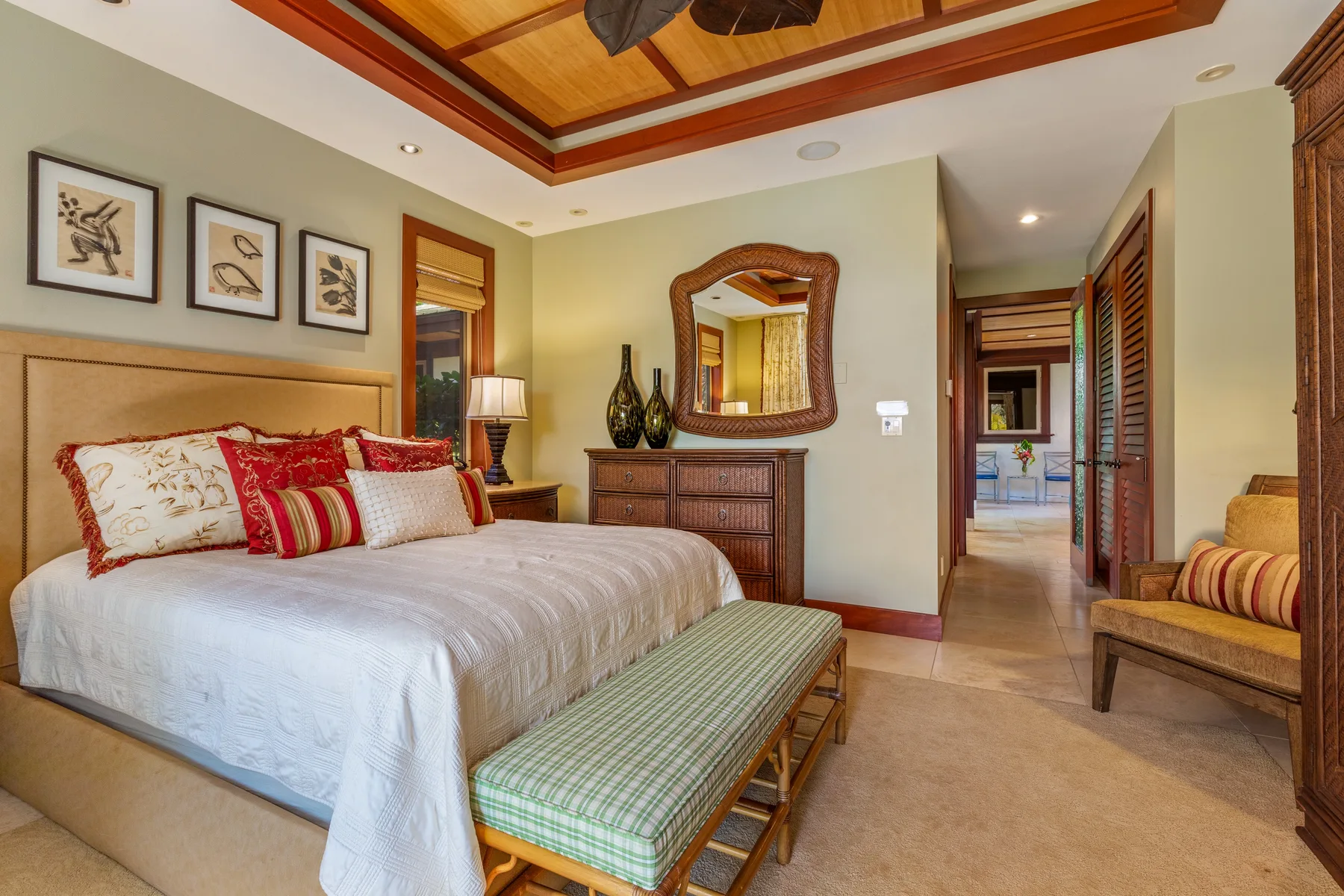 A bedroom with a made bed, a bench at its foot, and a dresser beneath a mirror.