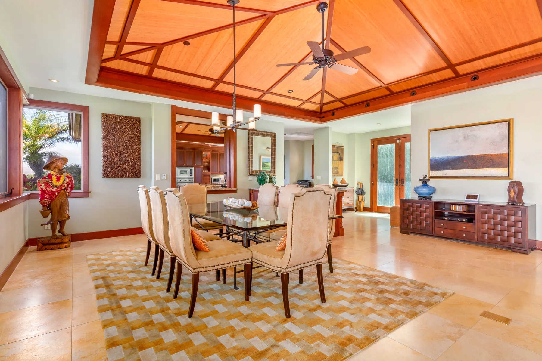 A dining room with a long table and upholstered seating beneath a wood-paneled ceiling.