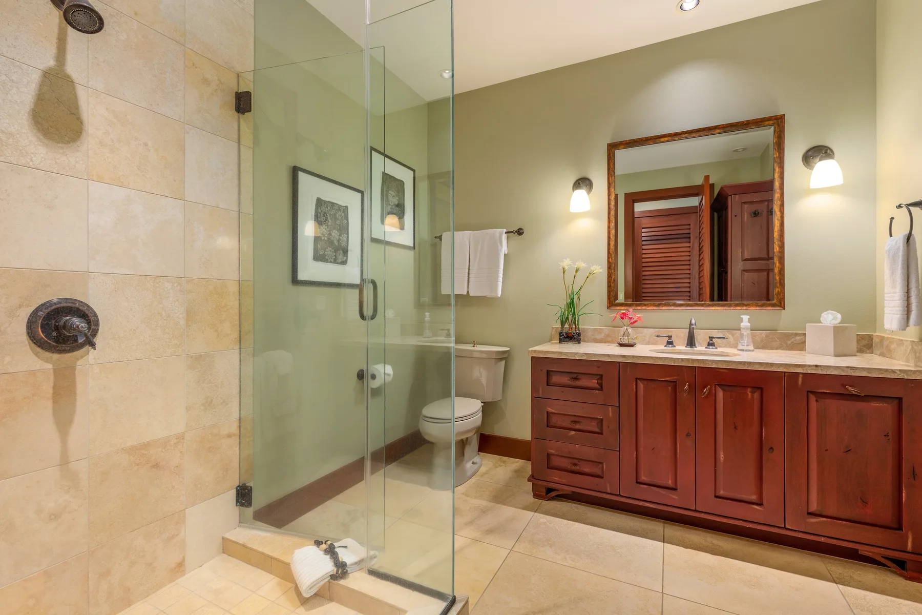 A bathroom with a glass shower and a wooden vanity beneath a mirror.