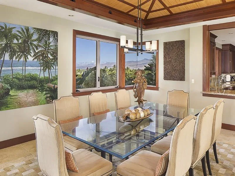 A dining area with a glass table and windows overlooking a green landscape.