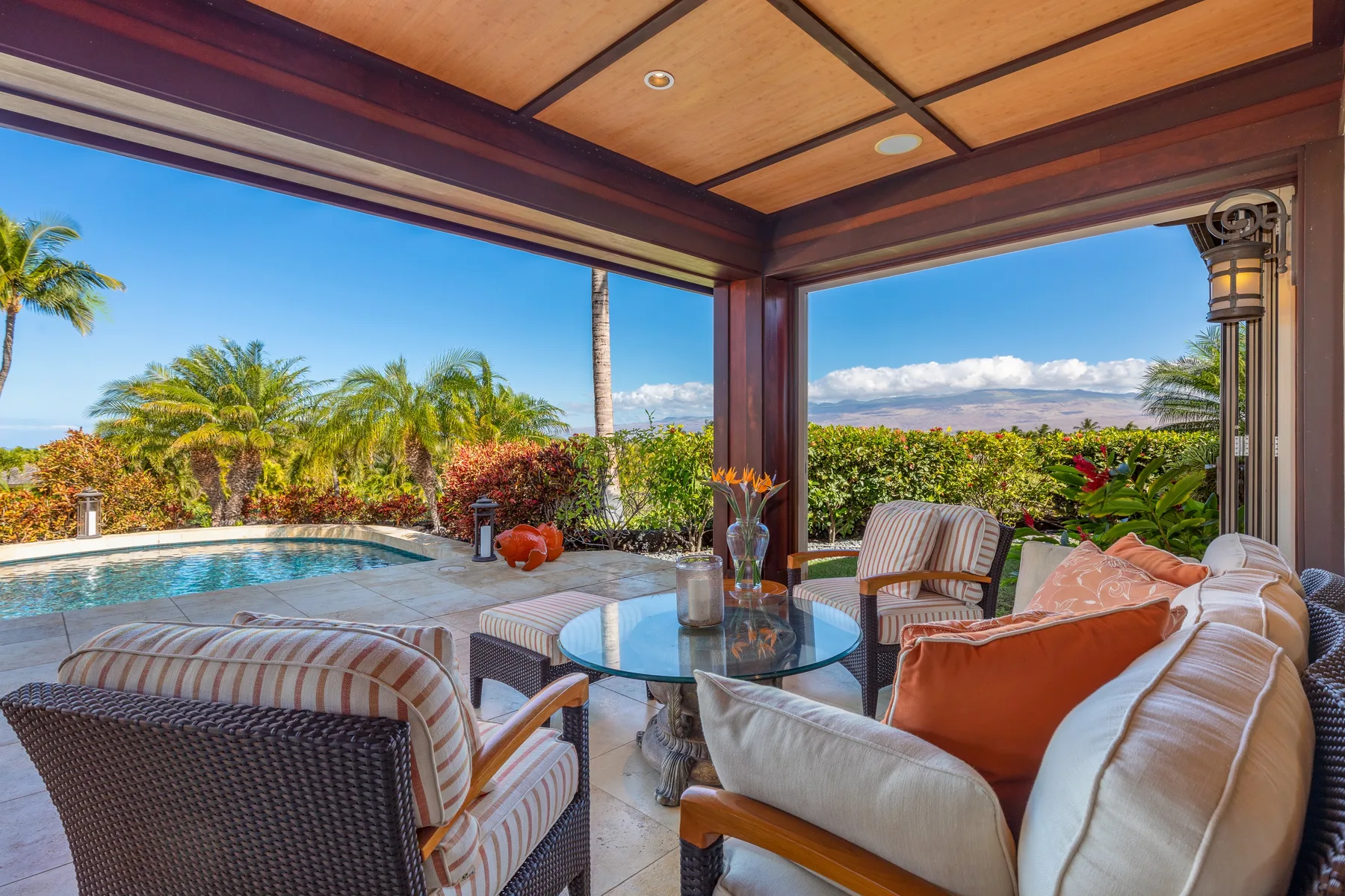 A covered outdoor seating area overlooks a pool and tropical greenery.