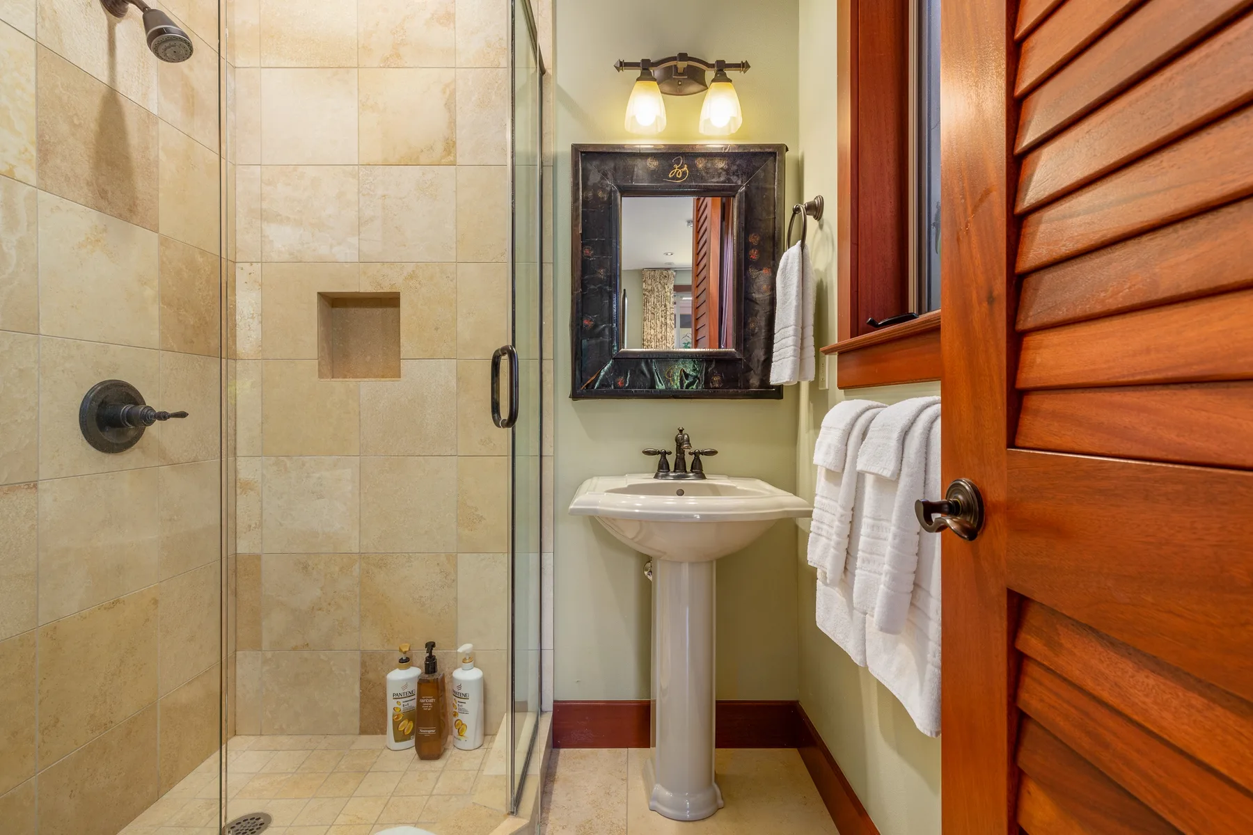 A tiled bathroom with a glass shower and pedestal sink.