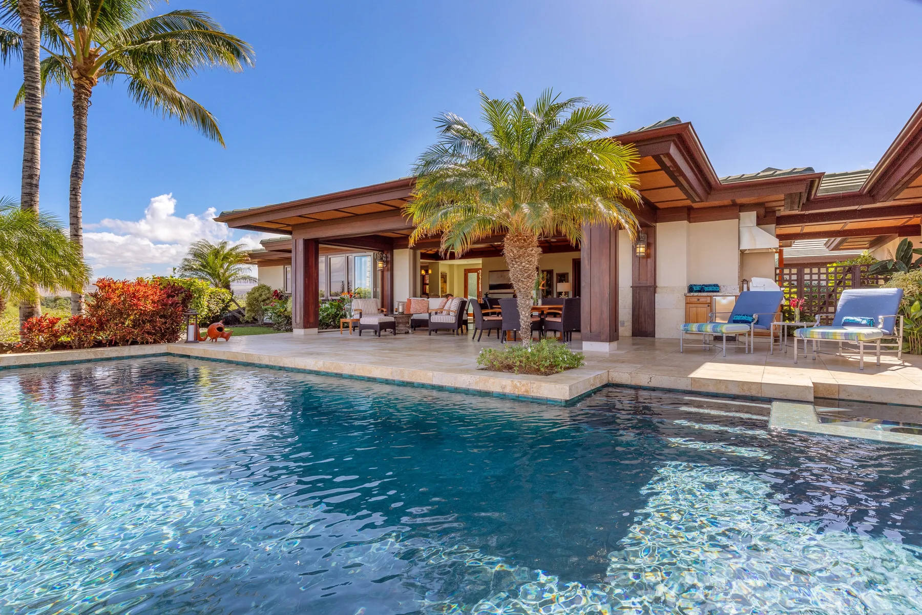 A swimming pool sits beside a covered patio with outdoor seating.