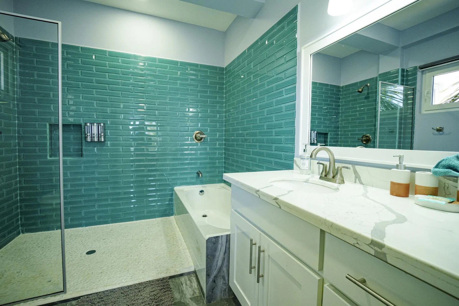 A tiled bathroom with a bathtub, glass shower screen, and long vanity.