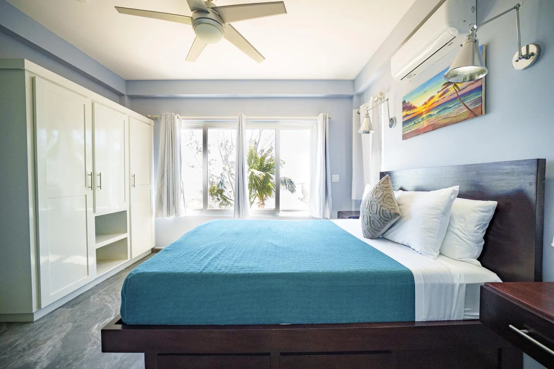 A bright bedroom with a bed dressed in turquoise bedding and white pillows.