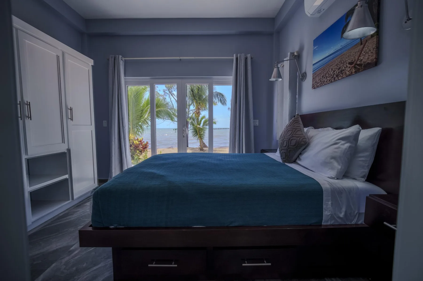 A bedroom with a bed facing glass doors that open onto a palm-lined view.
