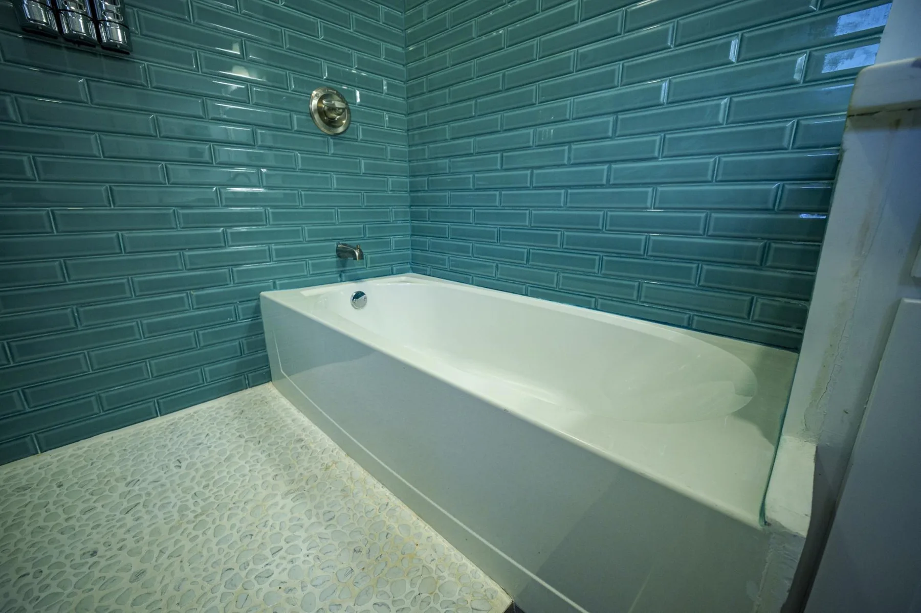 A bathroom with a bathtub set against teal tiled walls.