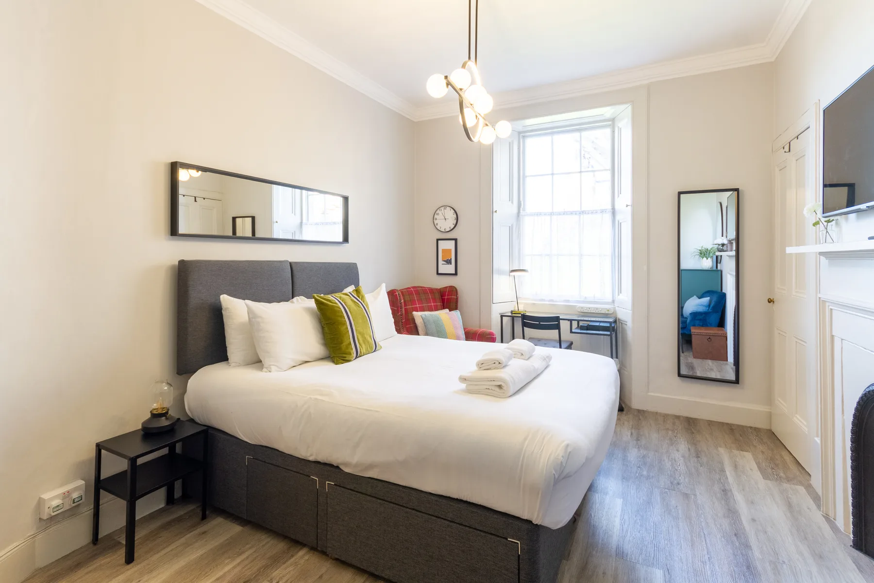 Un dormitorio luminoso con una cama bien tendida y una ventana grande.