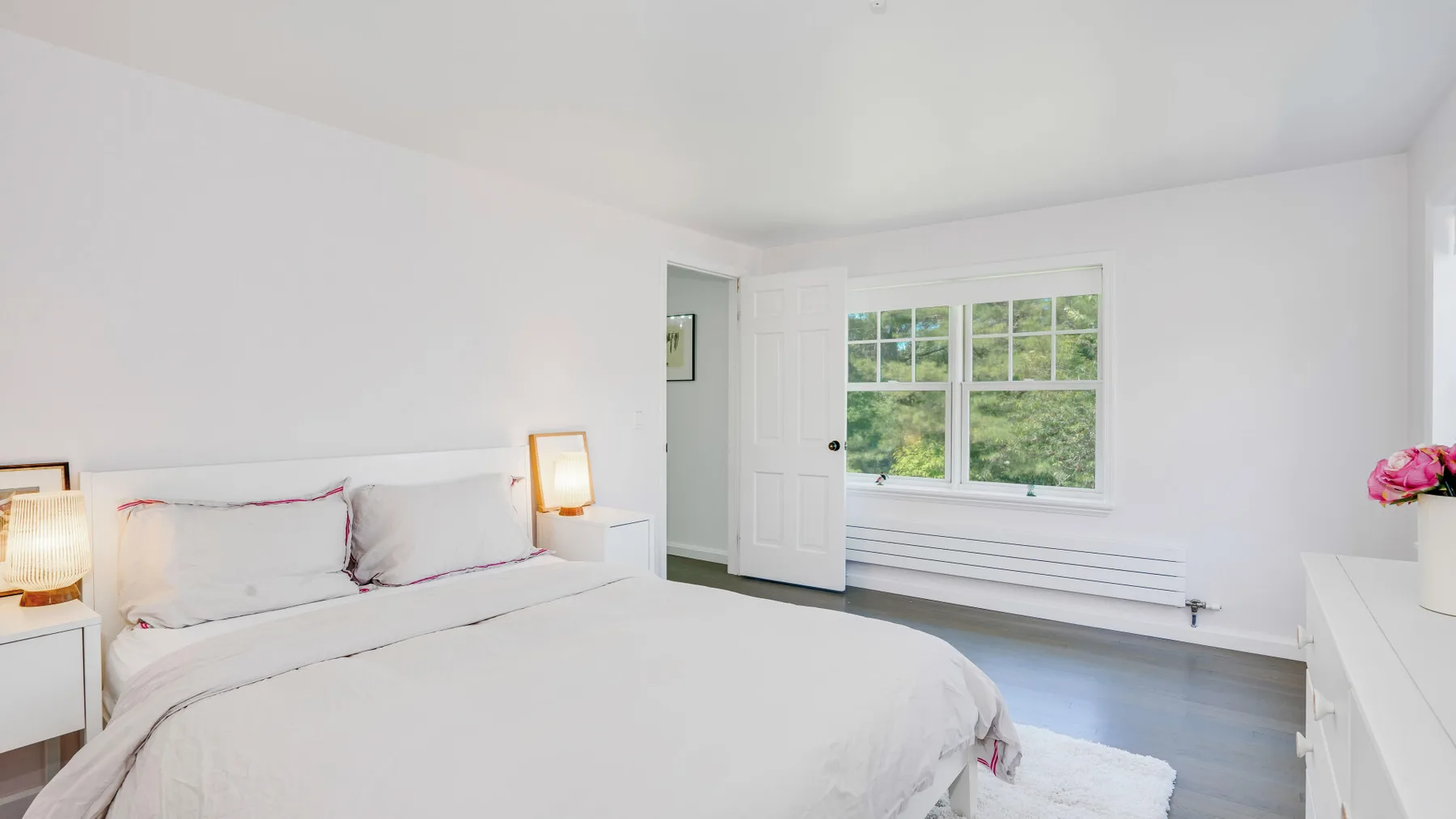 Un dormitorio luminoso con una cama junto a una ventana y una cómoda blanca.