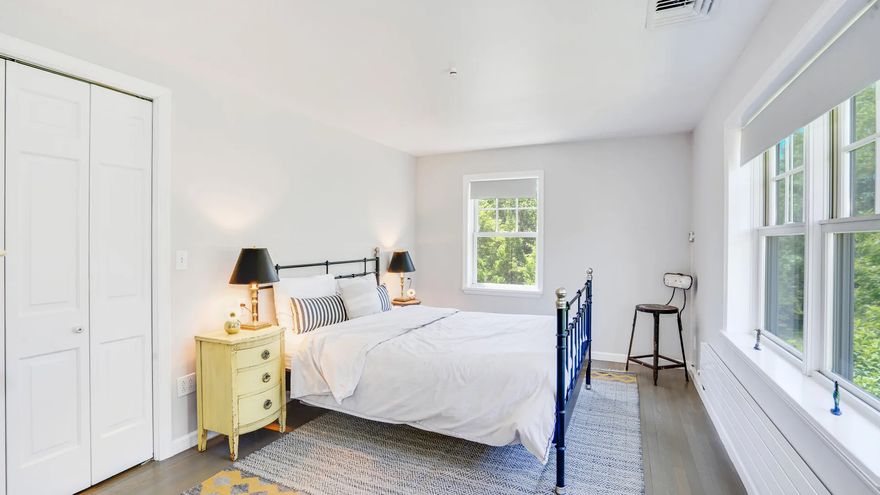Un dormitorio luminoso con una cama, mesitas de noche y grandes ventanas.