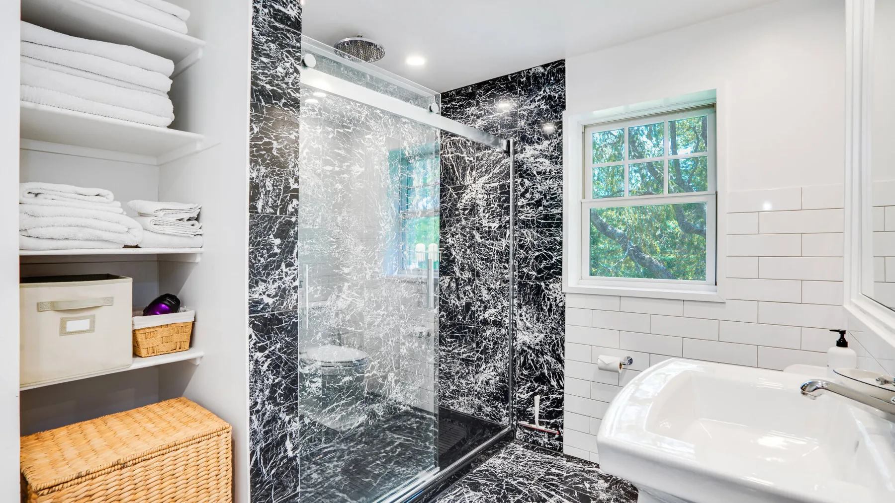 Un baño luminoso con ducha de vidrio, bañera y estantes para toallas.