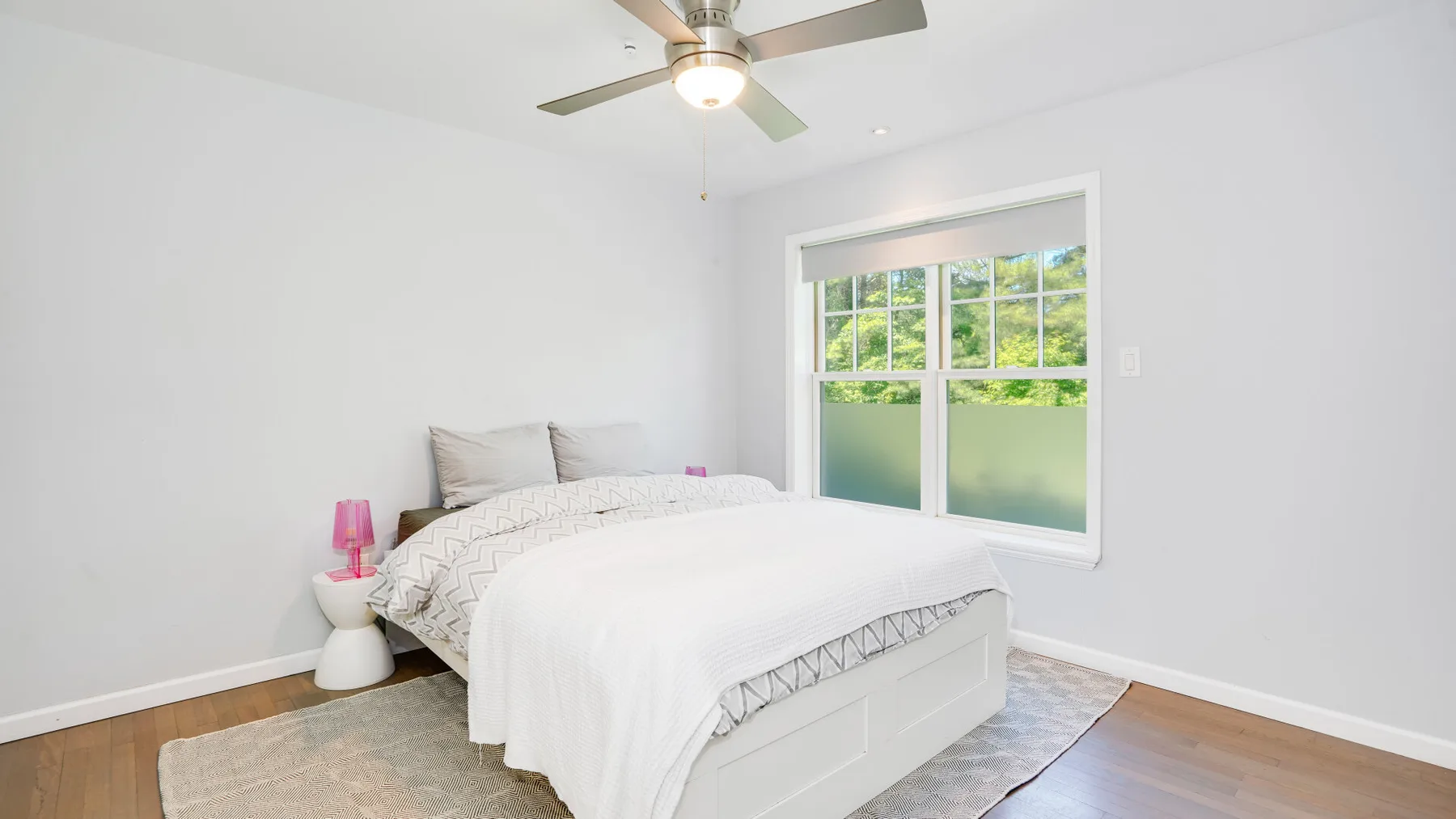 Un dormitorio luminoso con una cama bien tendida junto a una ventana grande.