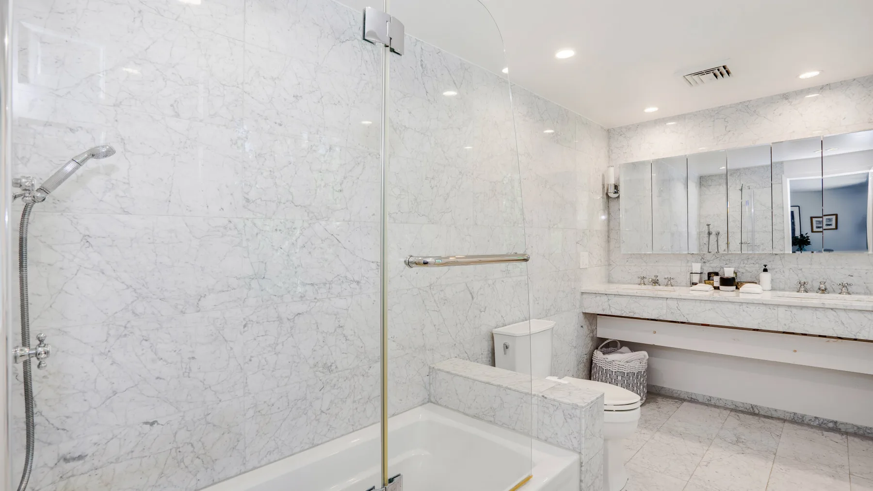 Un baño luminoso con una ducha de vidrio y un tocador largo.