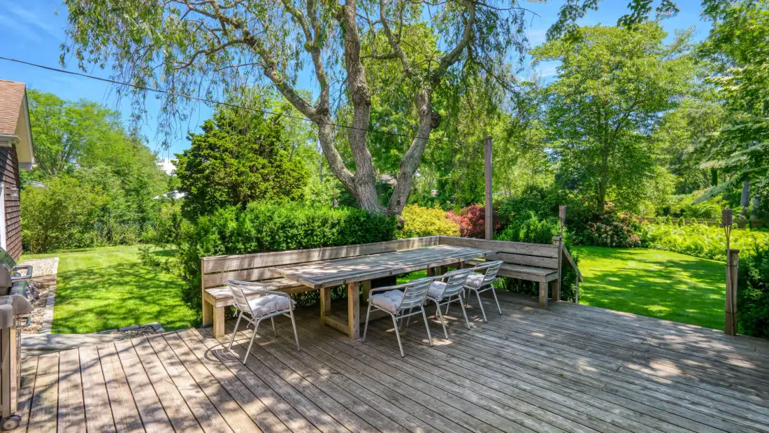 Una terraza de madera con mesa y sillas de comedor al aire libre da a un jardín frondoso.