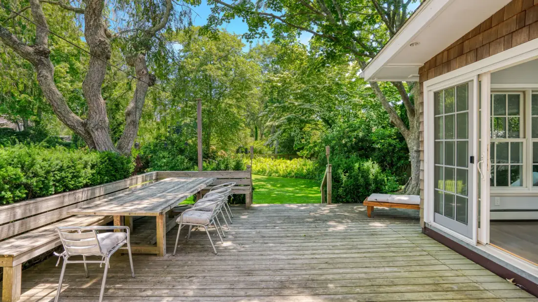 Una terraza de madera junto a la casa da a un jardín frondoso.