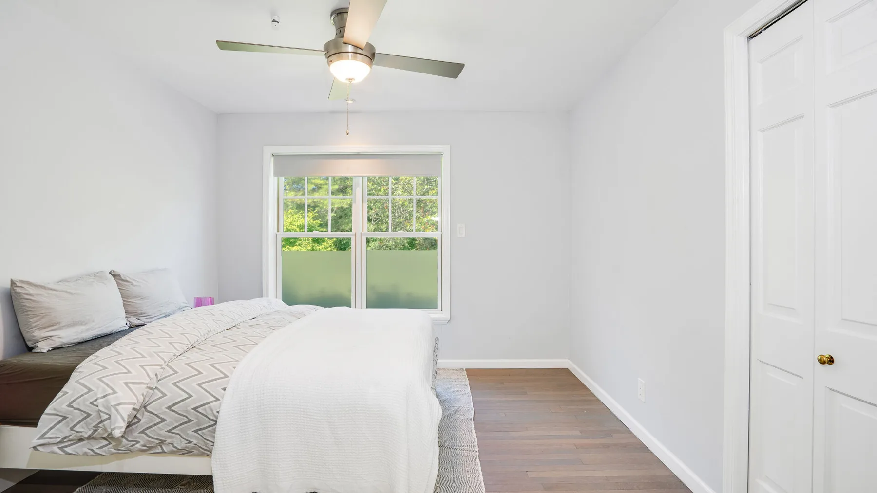 Un dormitorio luminoso con una cama, una ventana y un ventilador de techo.