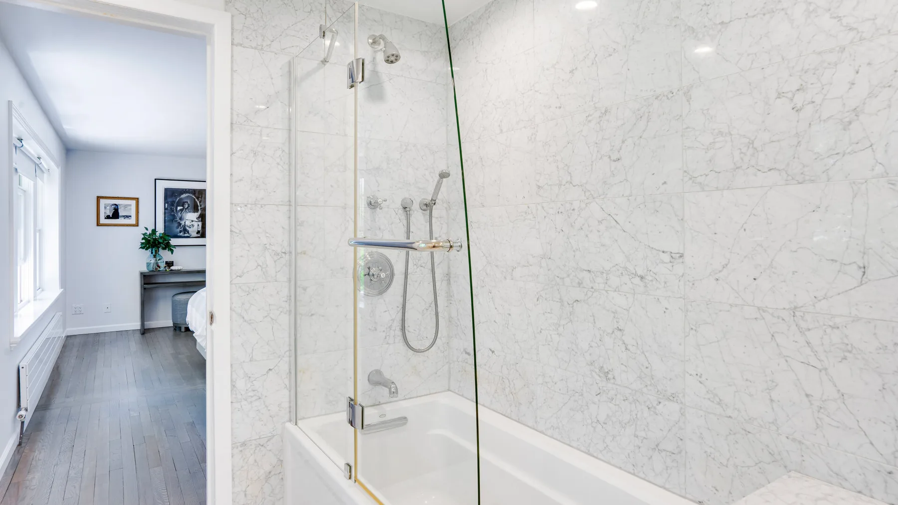 Un baño luminoso con bañera y mampara de vidrio junto a una pared con vetas marmoladas.