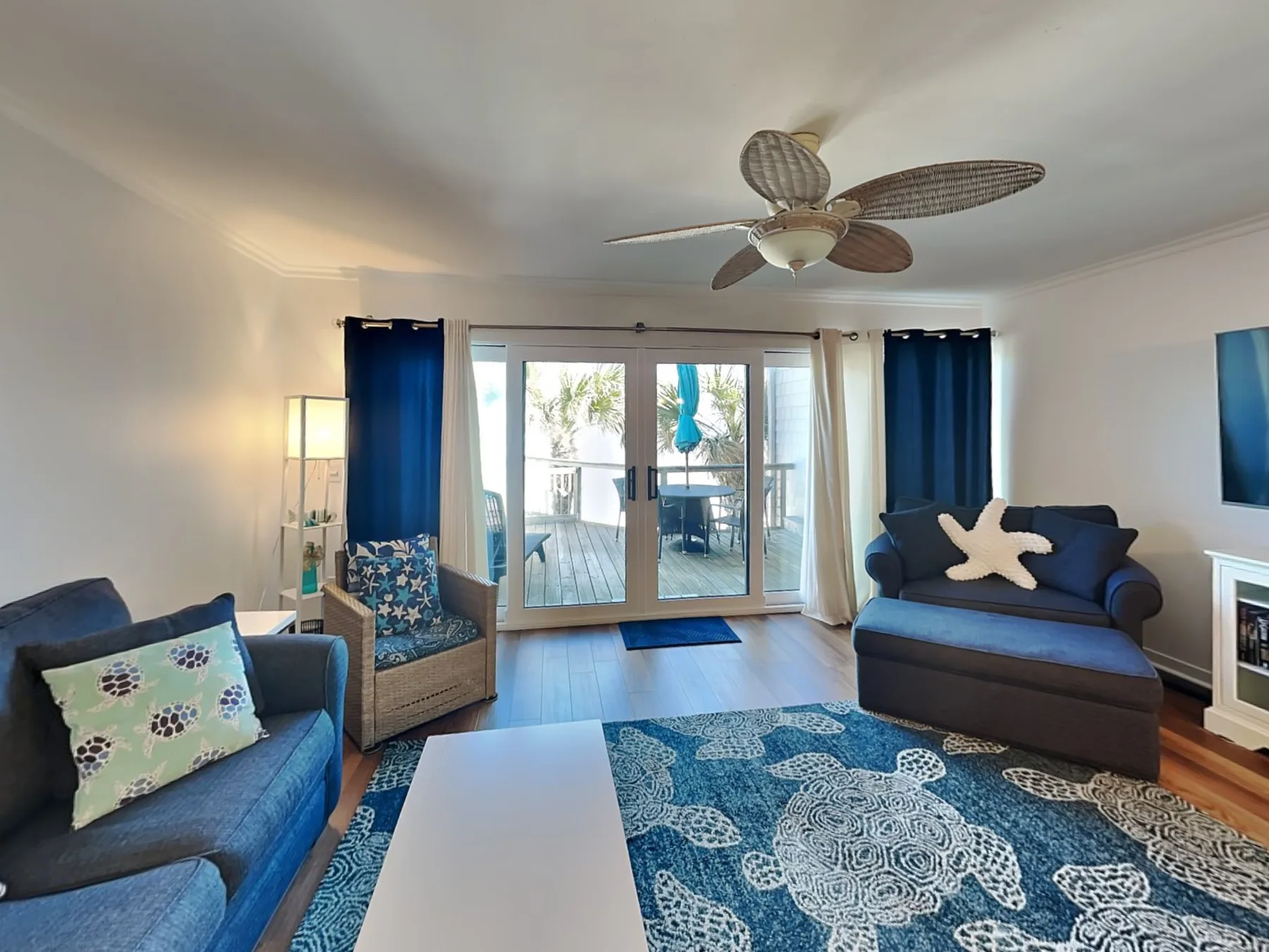 A living room with blue seating, a patterned rug, and glass doors opening to a balcony.