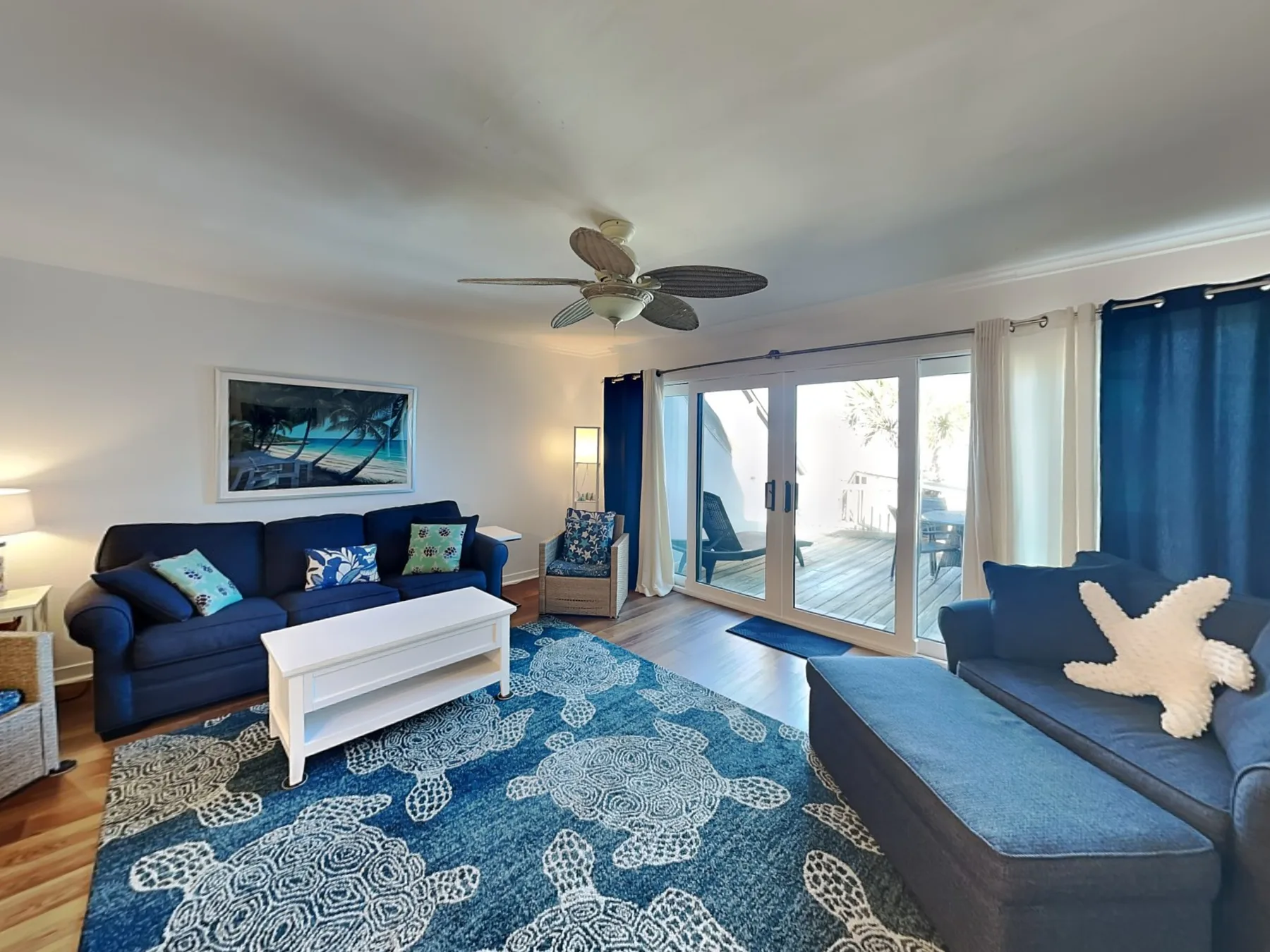 A living room with blue seating, a patterned rug, and sliding glass doors.