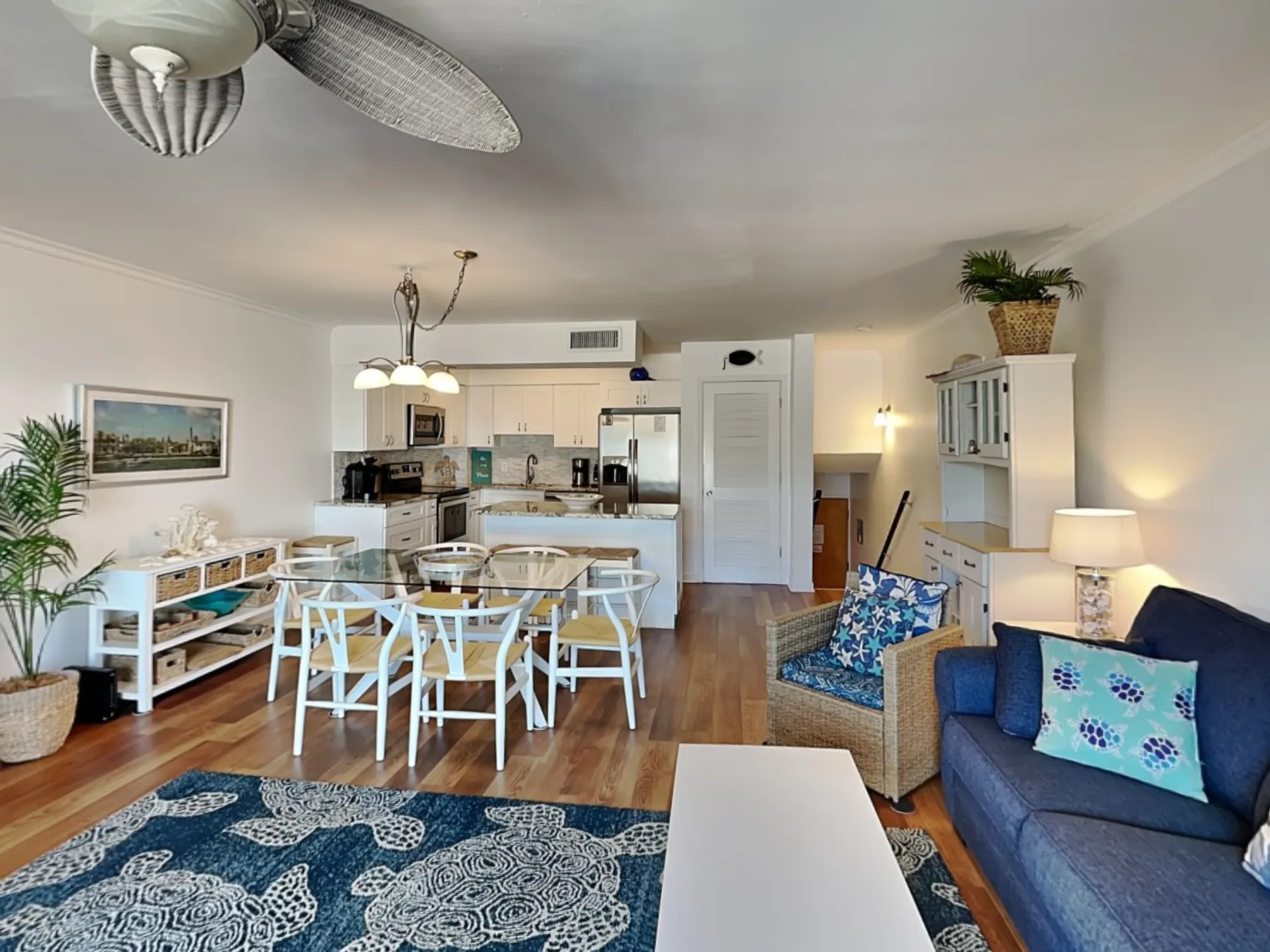 An open-plan living and dining area with a kitchen, blue seating, and a patterned rug.