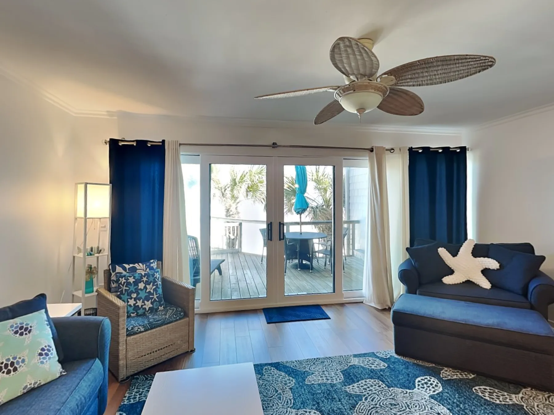 A living room with seating, blue curtains, and glass doors opening to a balcony.
