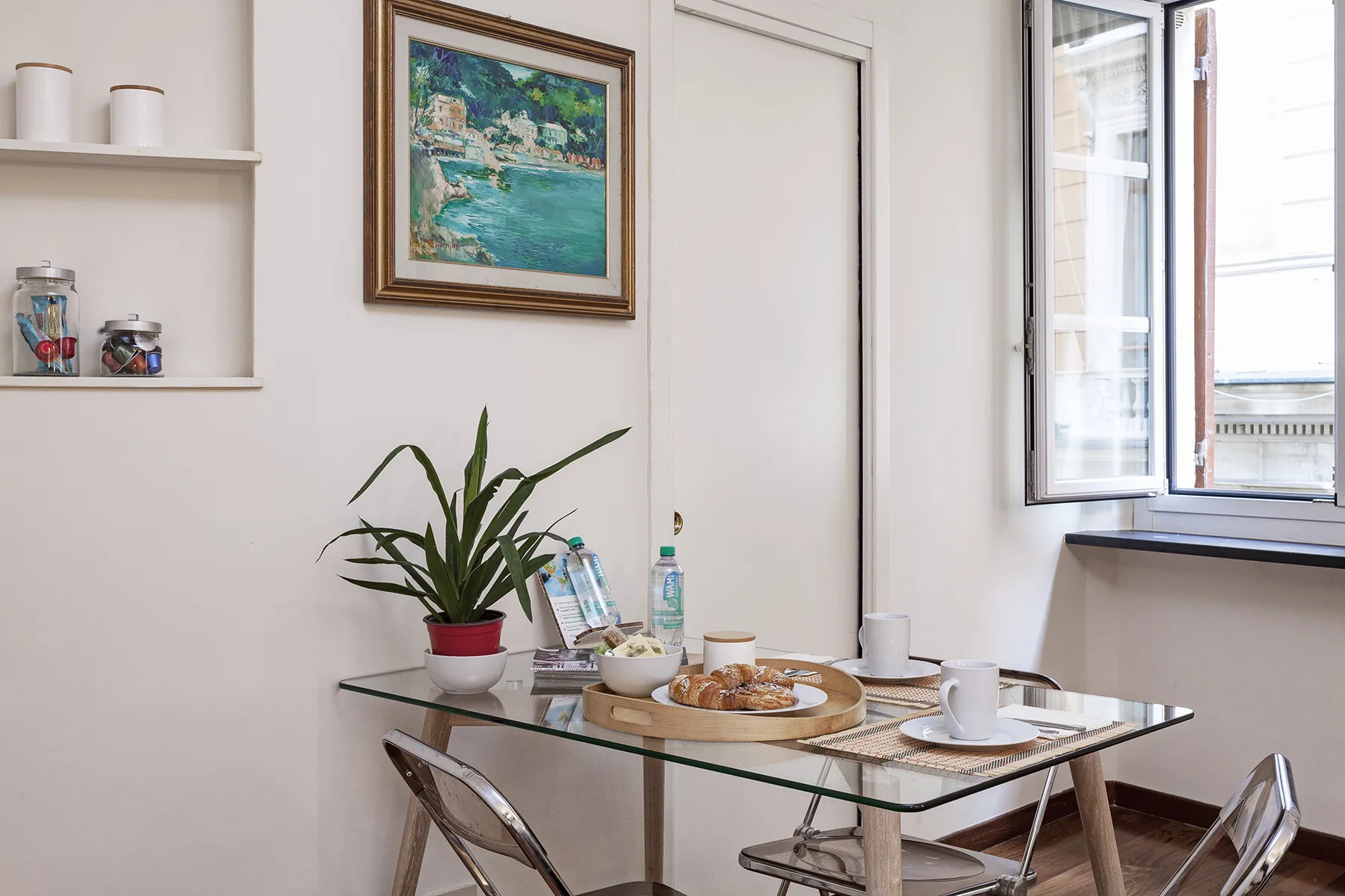 Un comedor luminoso con una mesa de cristal junto a una ventana abierta.