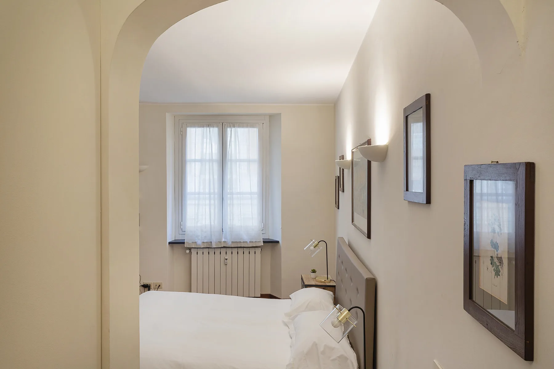 Un dormitorio con una cama bajo una ventana con cortinas translúcidas.