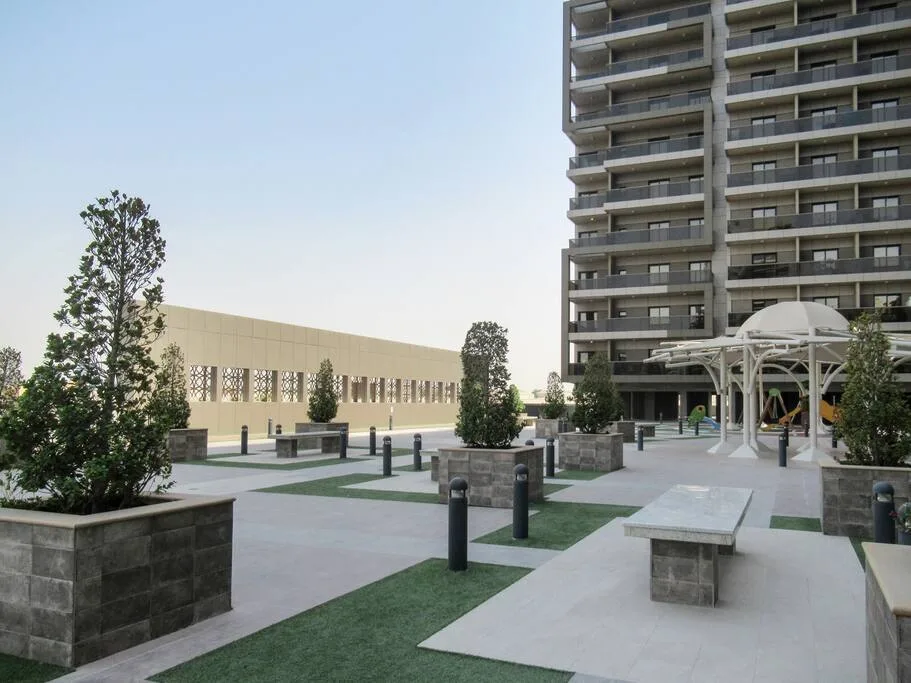 An outdoor courtyard with paved paths, planted areas, and a tall building.