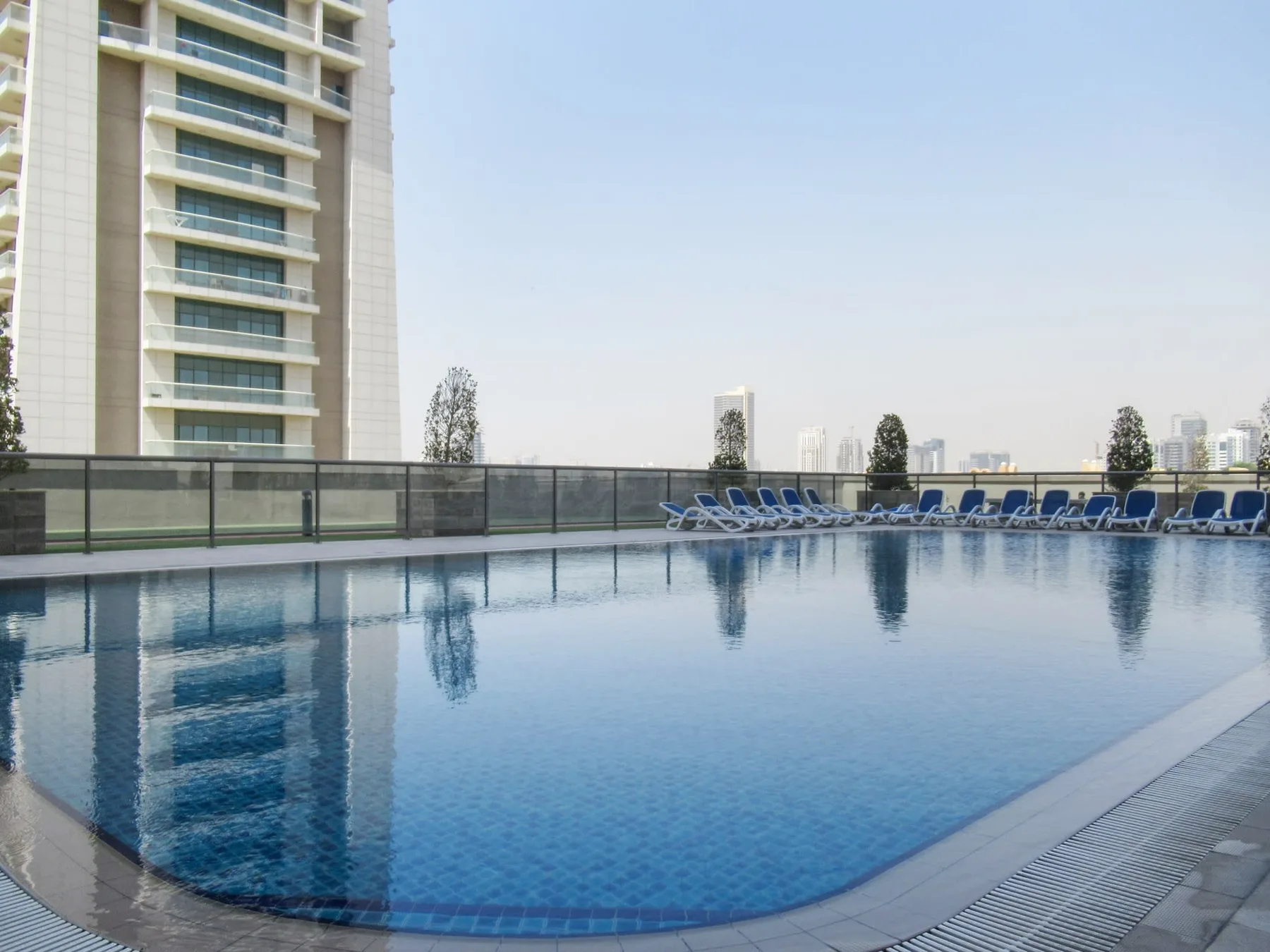 A swimming pool beside a high-rise building, with lounge seating along the far edge.