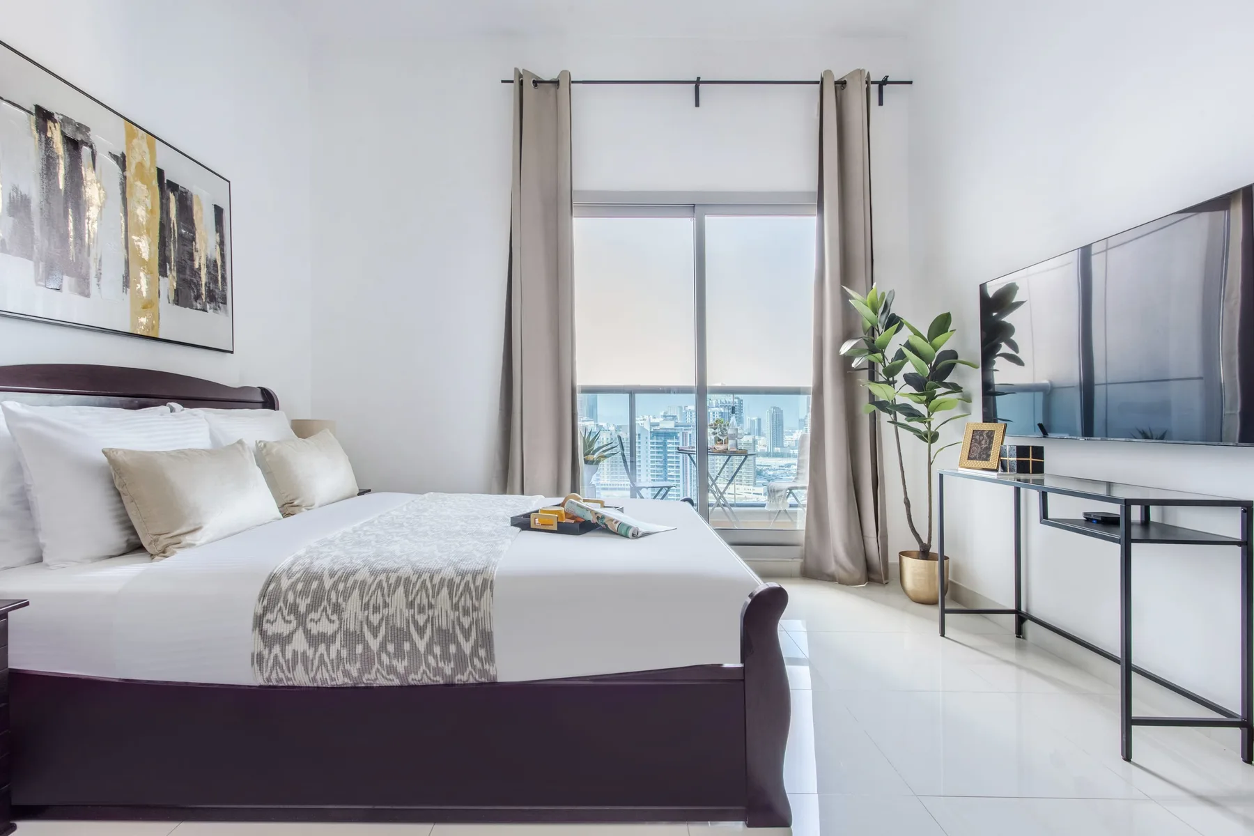A bedroom with a neatly made bed facing a window and city view.