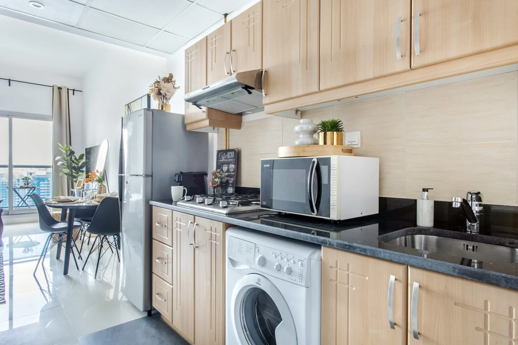 A bright kitchen with light wood cabinets, a washing machine, and a dining area.