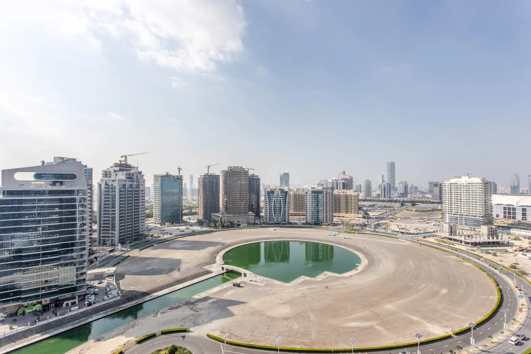 A city skyline surrounds a broad circular roadway and a small green pond.