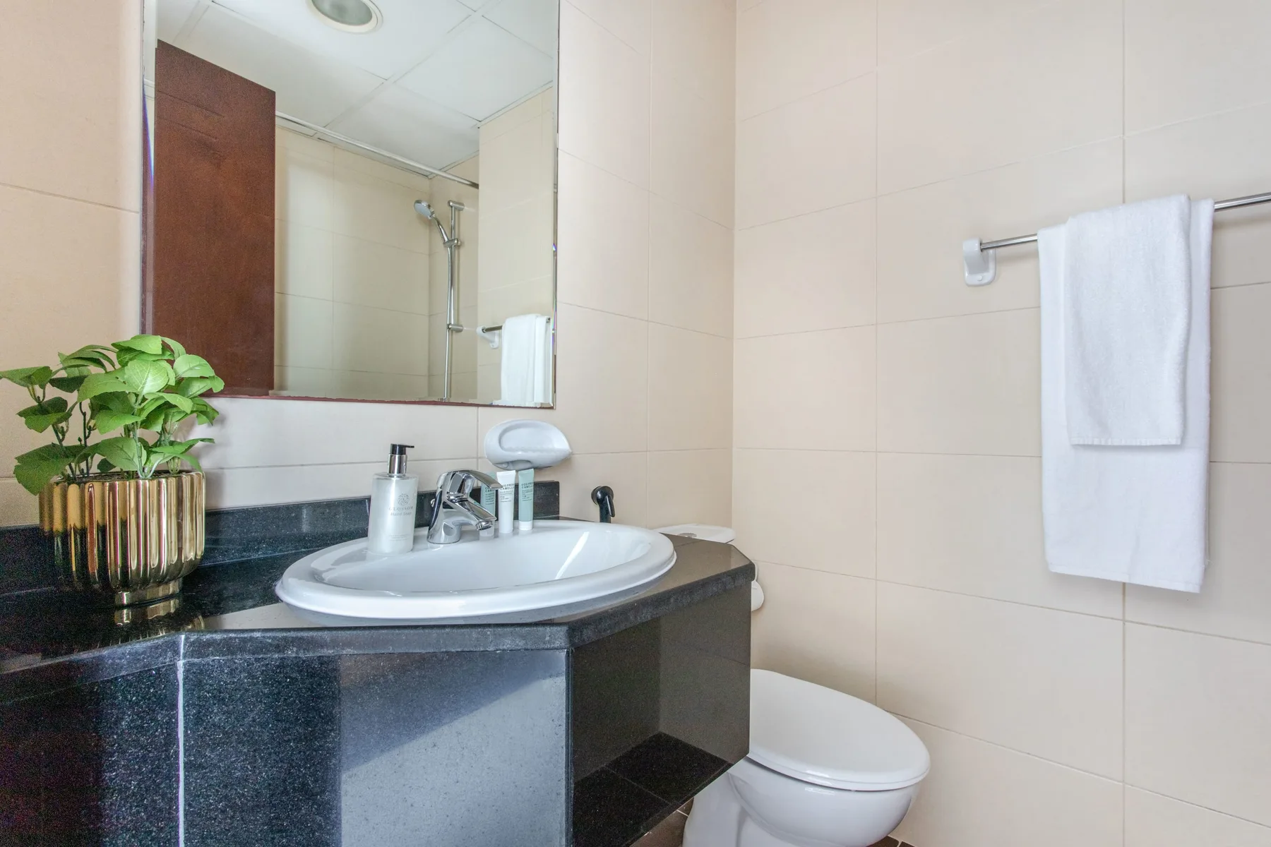 A tiled bathroom with a sink, mirror, and towel hanging on the wall.