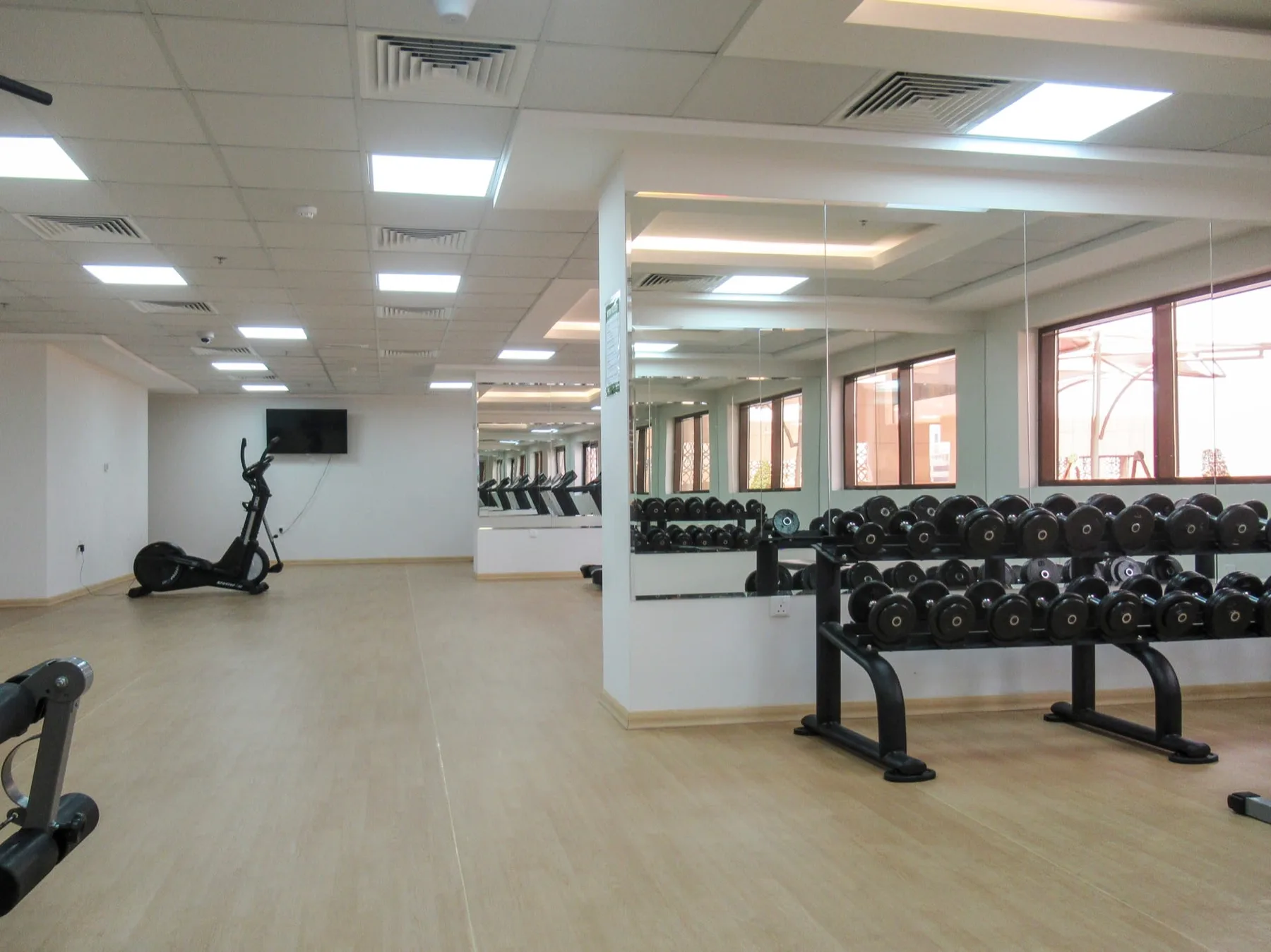 A gym with rows of dumbbells beside a mirrored wall.