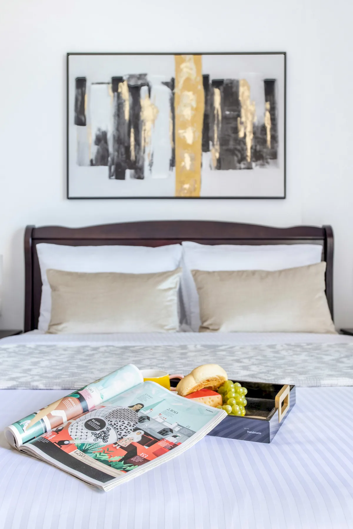 A bedroom with a neatly made bed, abstract artwork, and a tray of fruit.