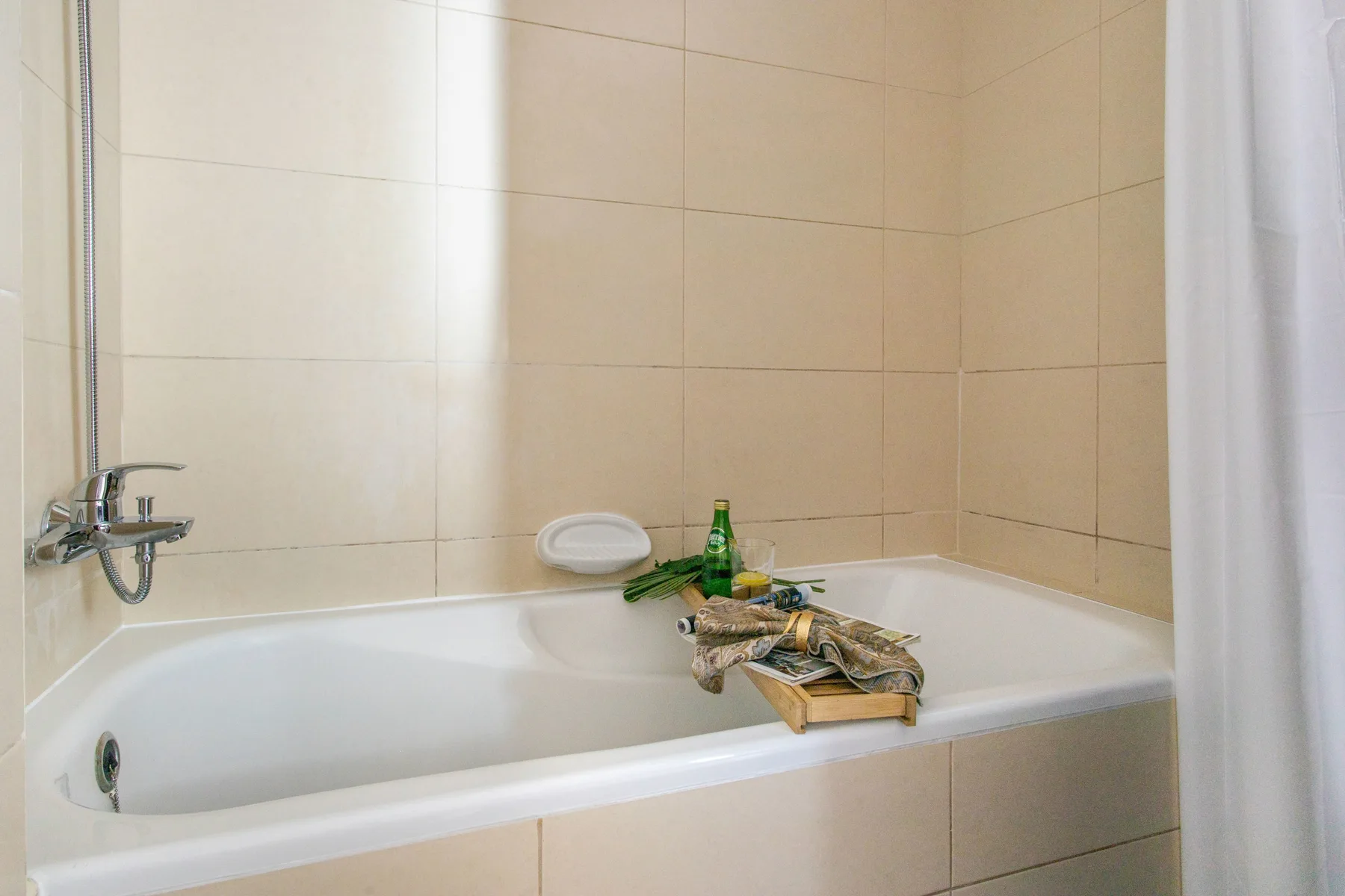 A tiled bathroom with a bathtub and wall-mounted faucet.