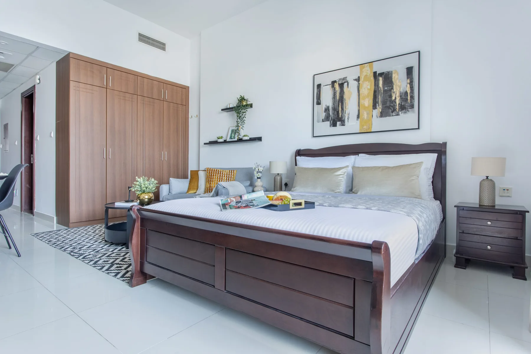 A bright bedroom with a large bed, wooden wardrobe, and framed wall art.