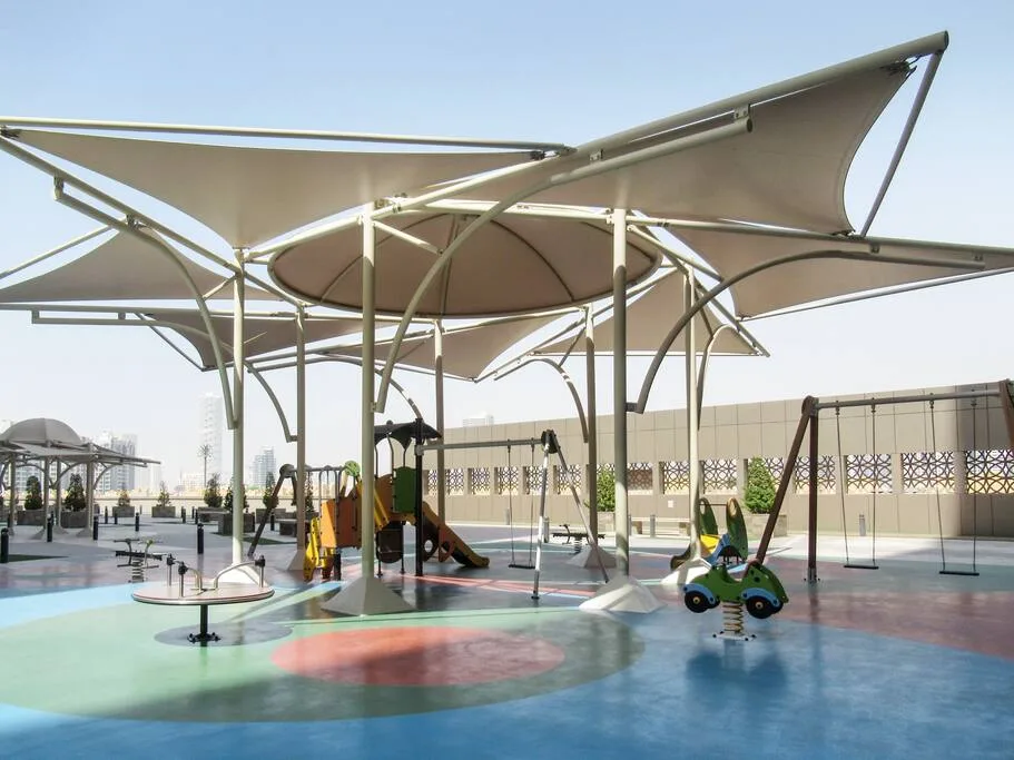 A shaded outdoor playground has colorful play equipment on a blue and green surface.