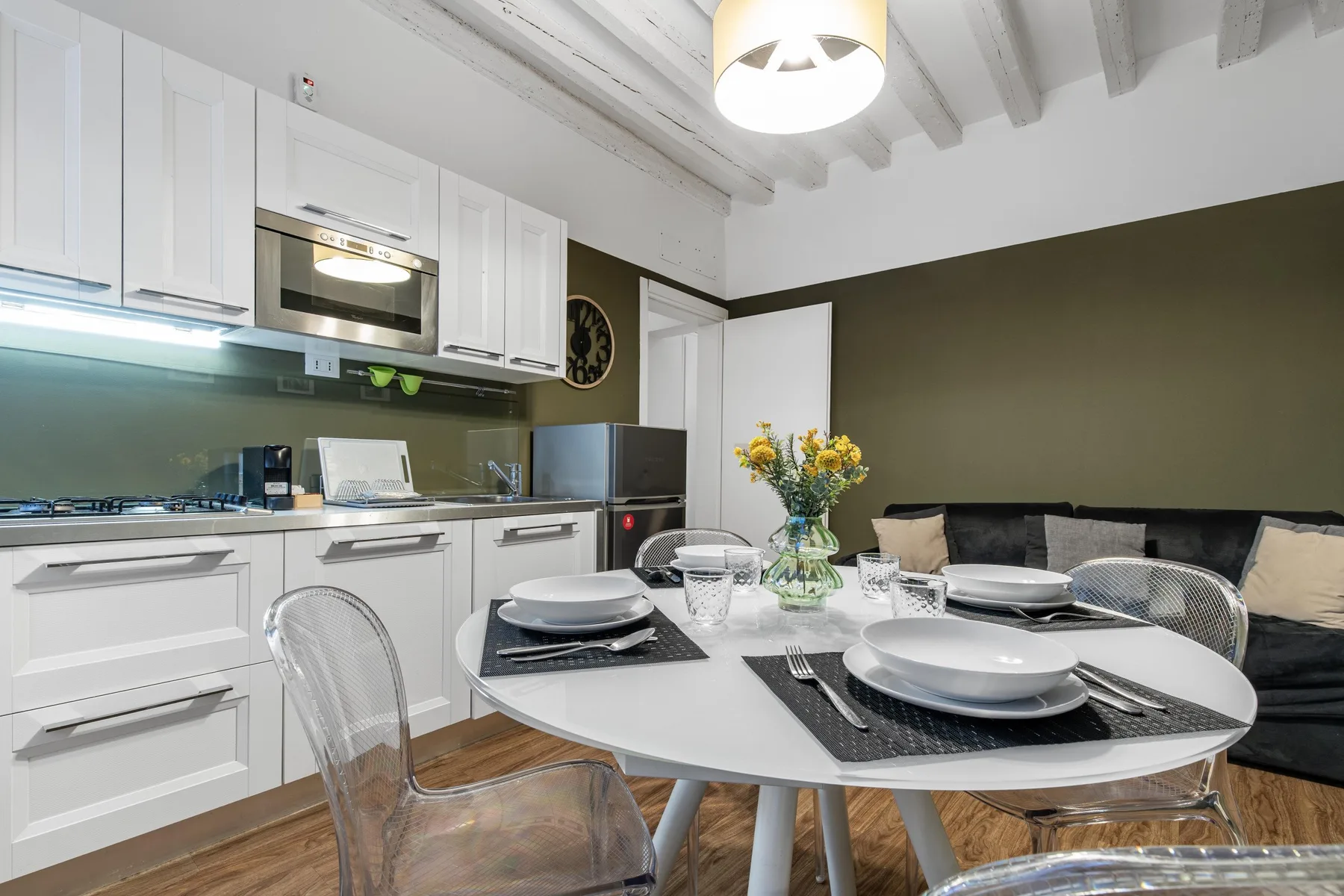 A dining table is set in a kitchen with white cabinets and a dark sofa.