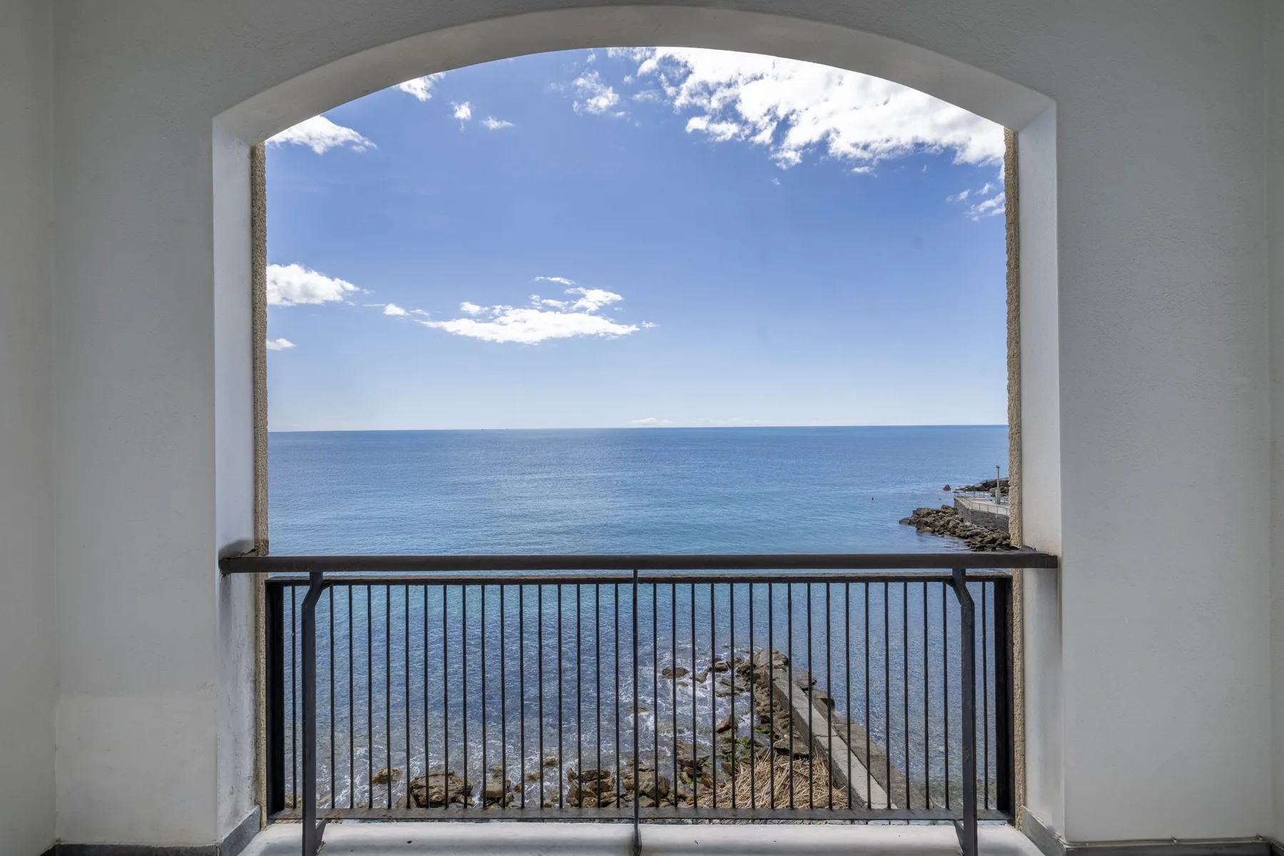 Una abertura arqueada enmarca una vista del mar y el cielo más allá de una barandilla.