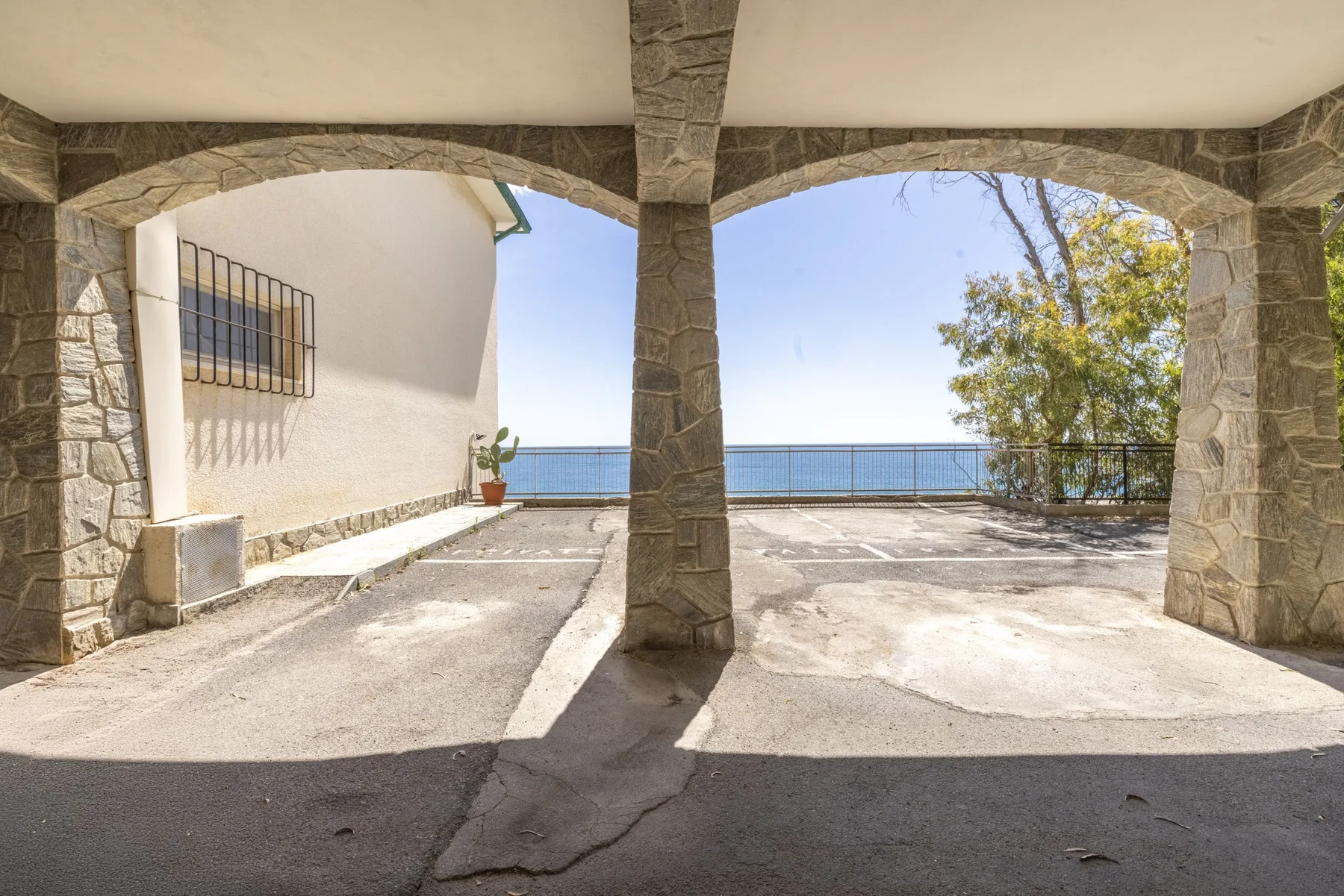Una terraza exterior con arcos de piedra da al agua, con un árbol junto a la barandilla.