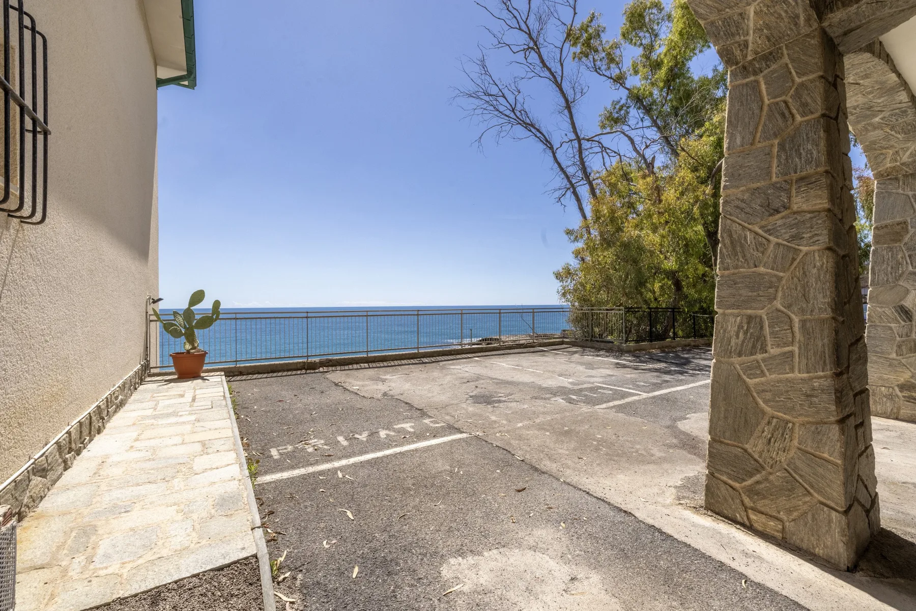 Una terraza exterior pavimentada da al mar, con una planta en maceta junto a la pared.