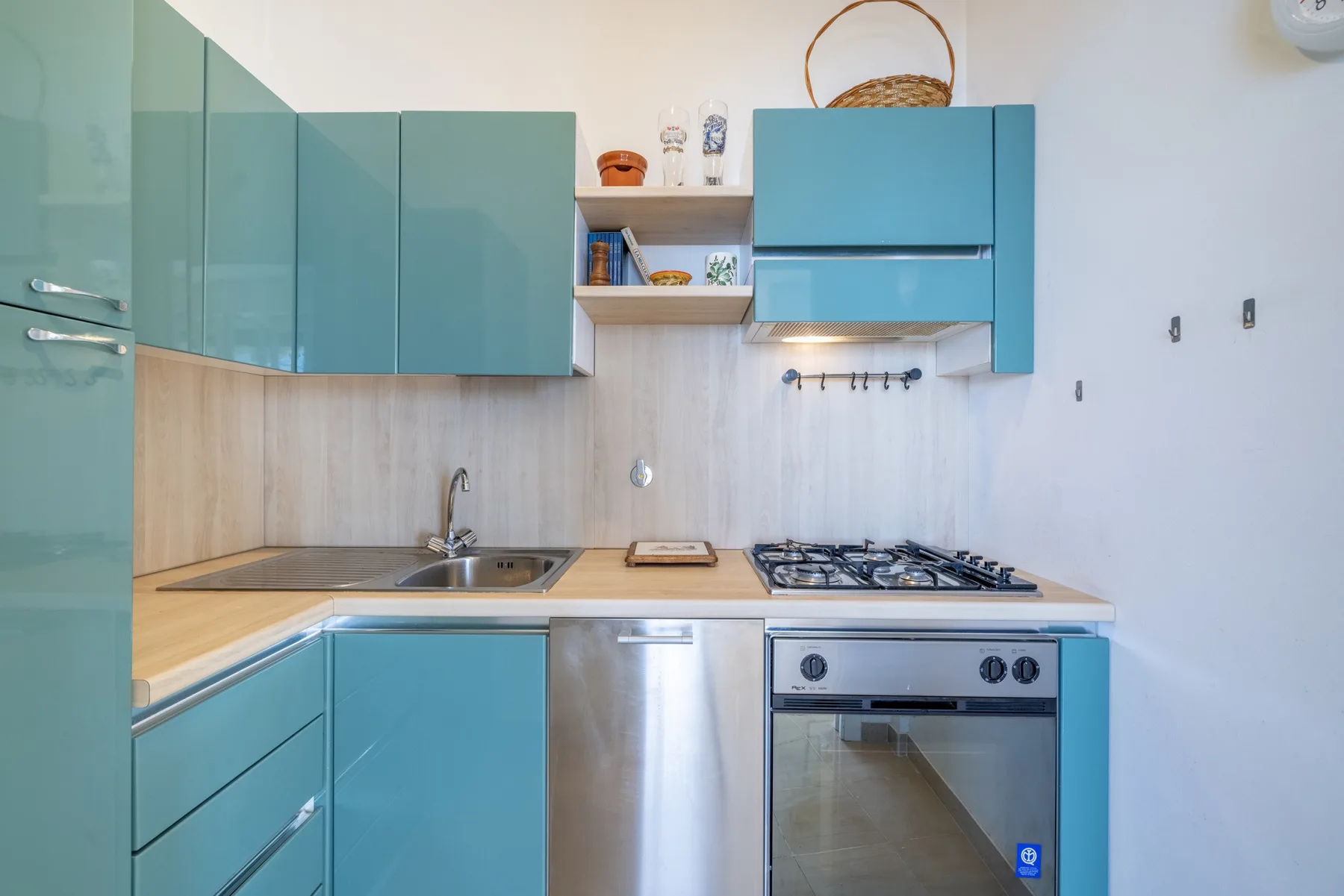 Una cocina compacta con gabinetes turquesa, un fregadero y un horno empotrado.