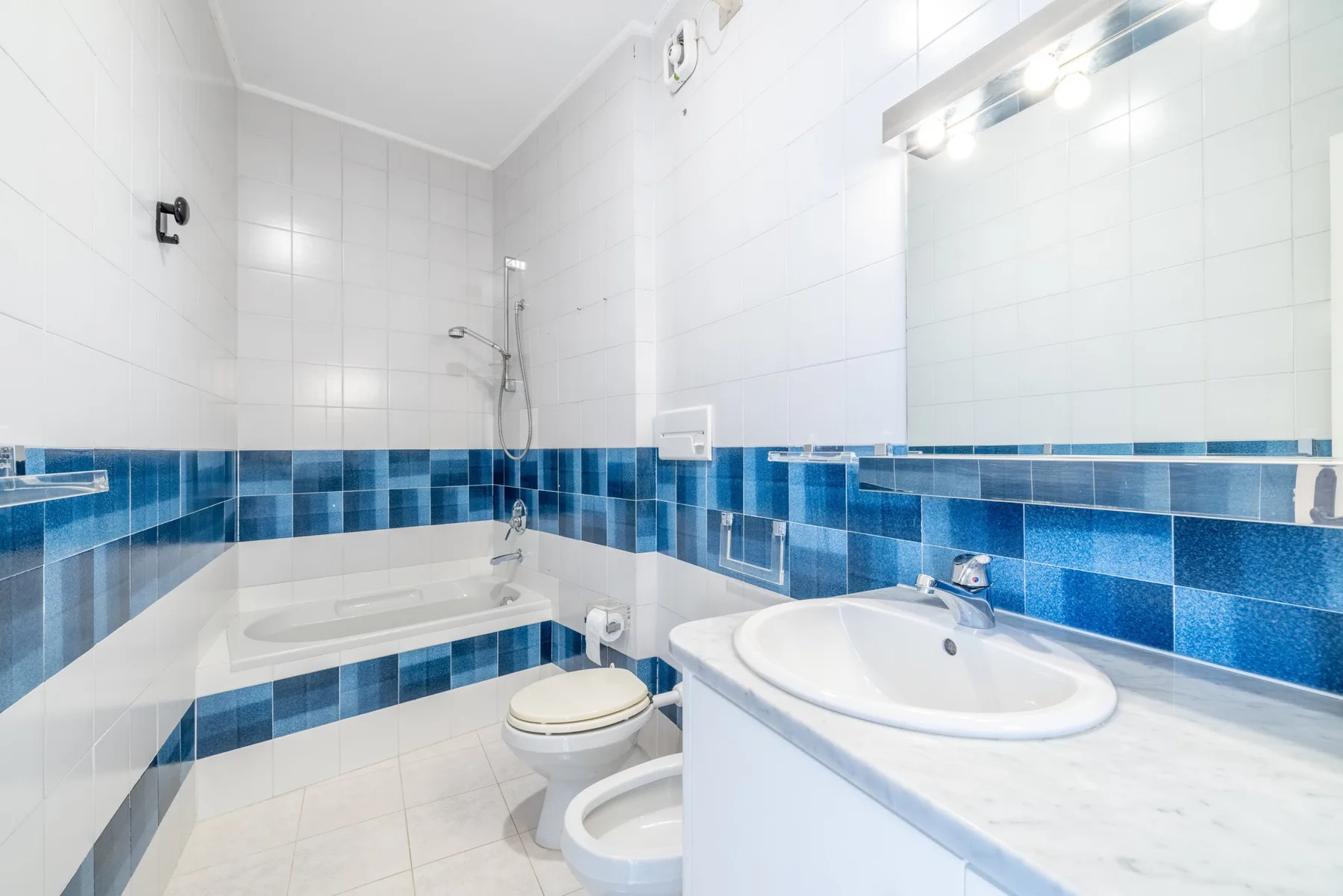 Un baño alicatado con bañera, inodoro y lavabo bajo un espejo grande.