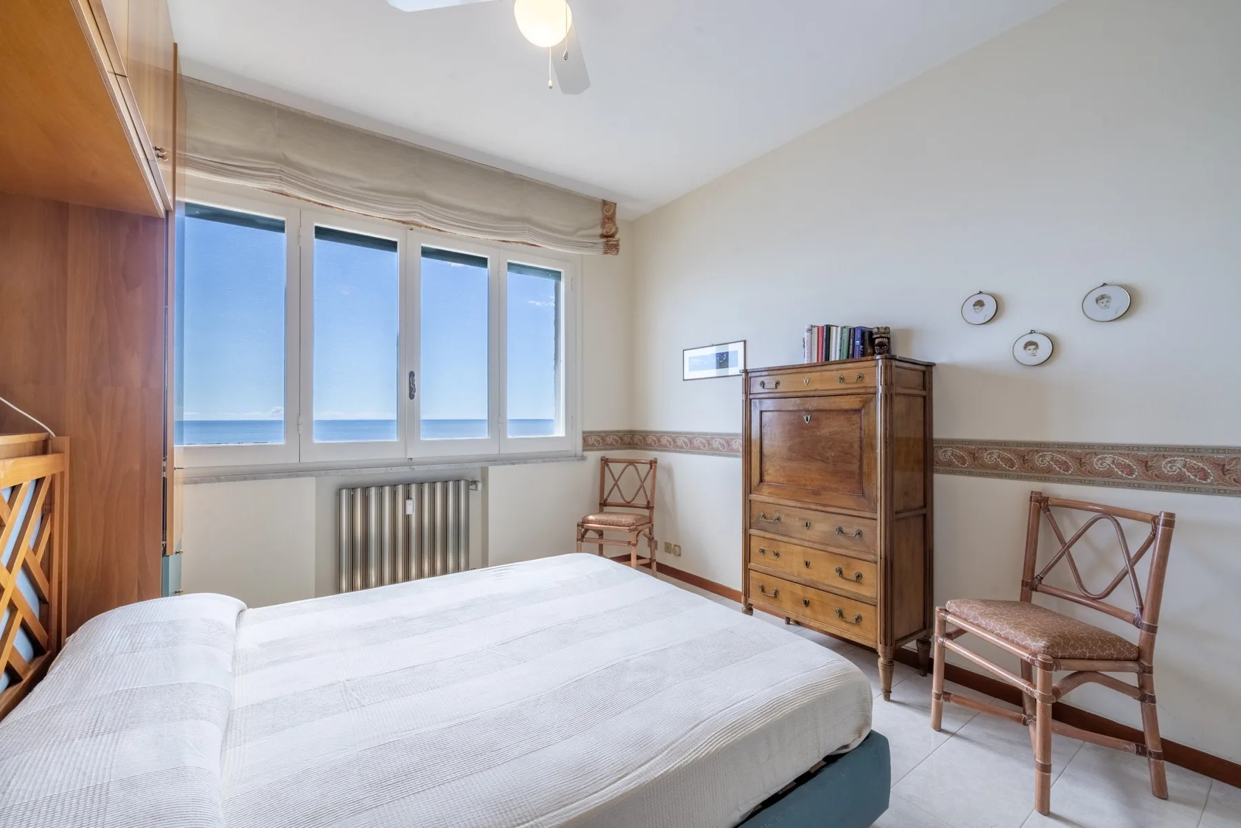 Un dormitorio con una cama, una cómoda alta de madera y ventanas con vista al agua.